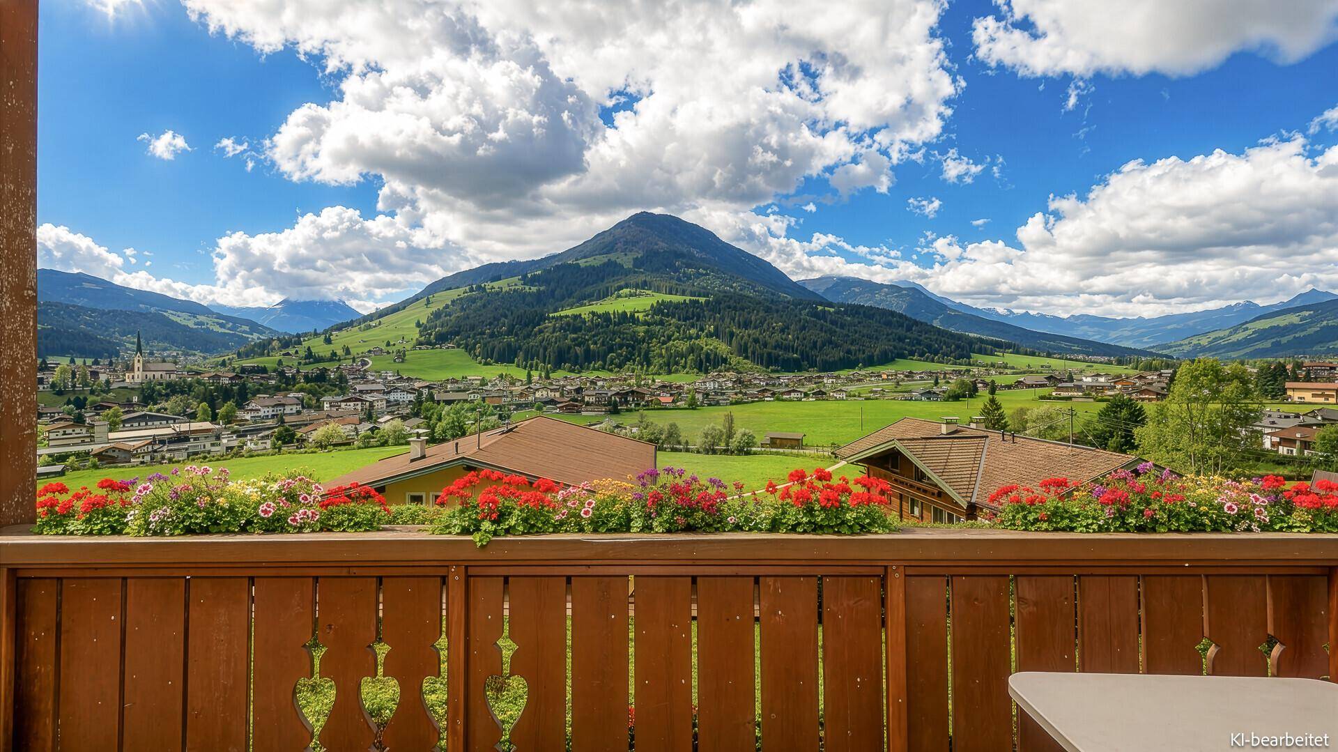 Malerischer Ausblick vom Balkon auf ein Dorf, grüne Hügel und die umliegende Bergwelt.