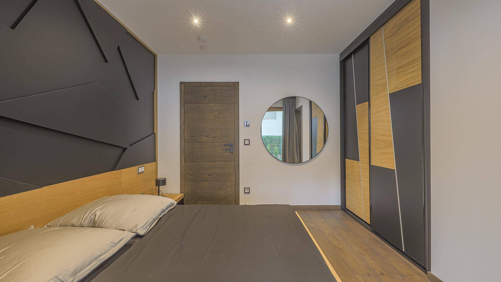 Schlafzimmer mit Holzboden, modernem Kleiderschrank und runden Spiegel als Dekoration.