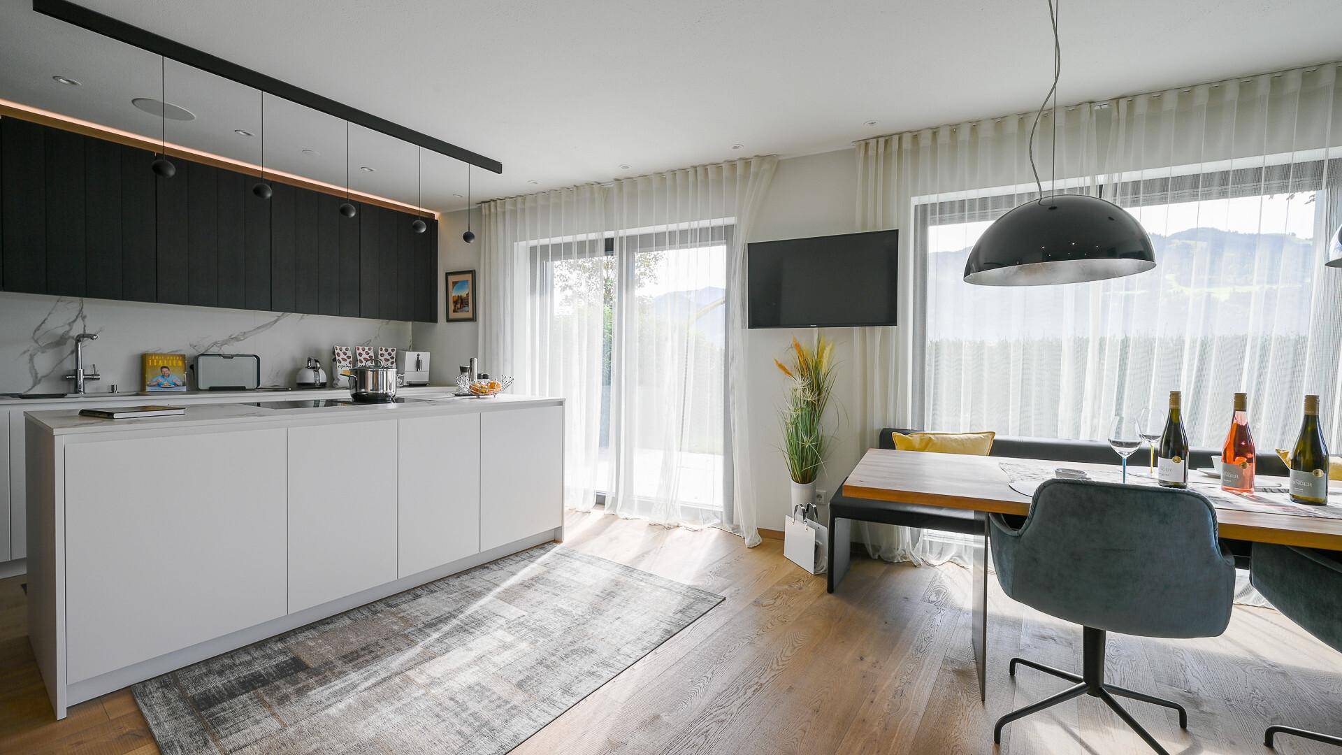 Moderne Küche mit weißer Kücheninsel, schwarzen Oberschränken und Essbereich mit Zugang zum Garten.