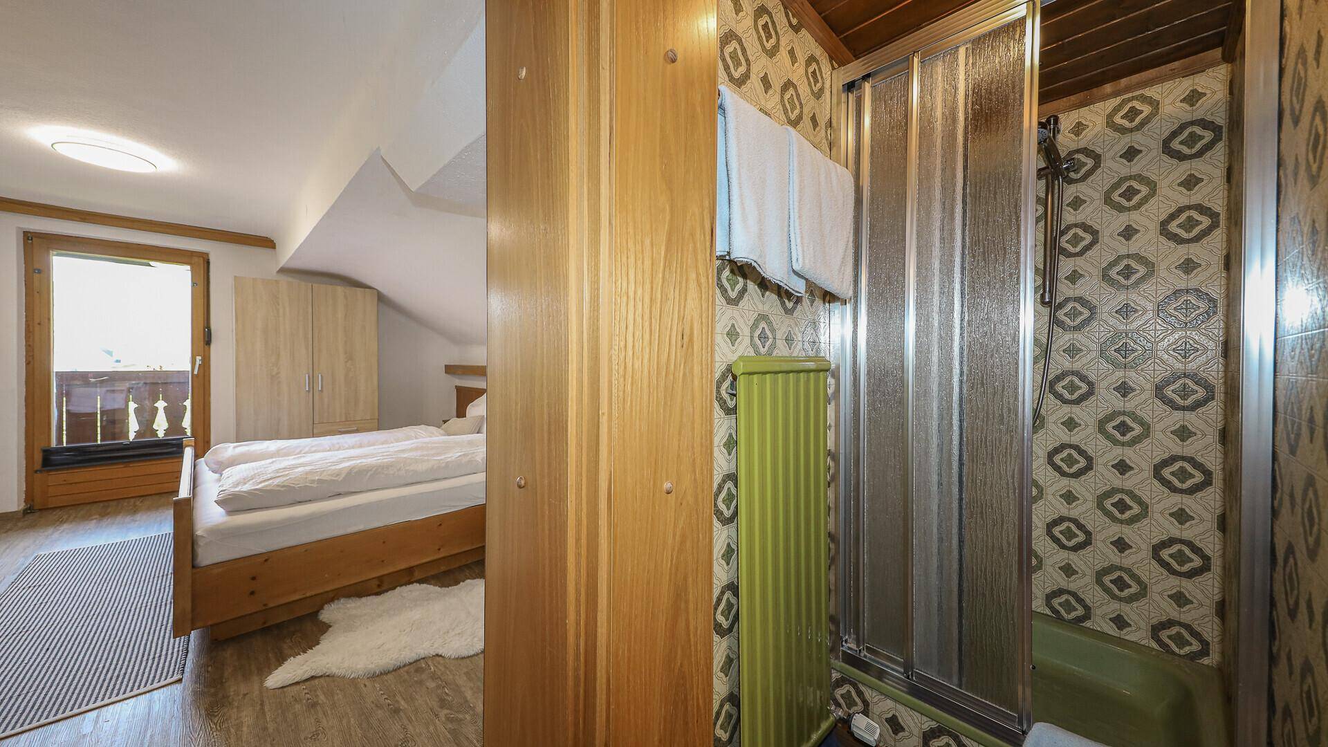 Schlafzimmer mit Balkonzugang, Doppelbett und integriertem Duschbereich.