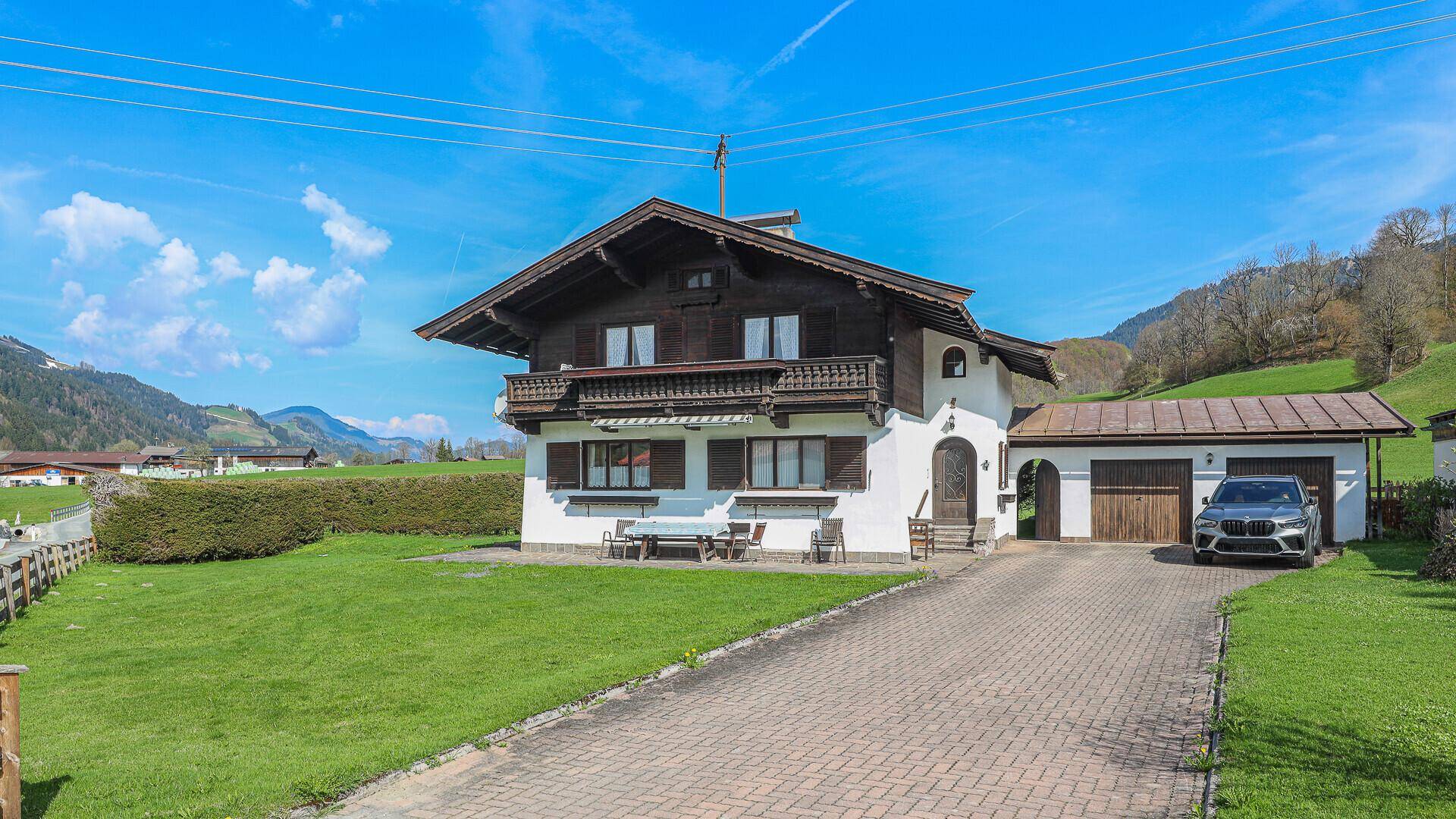 Alpines Wohnhaus mit weißer Fassade, Holzbalkonen und gepflegtem Vorgarten in ländlicher Umgebung.