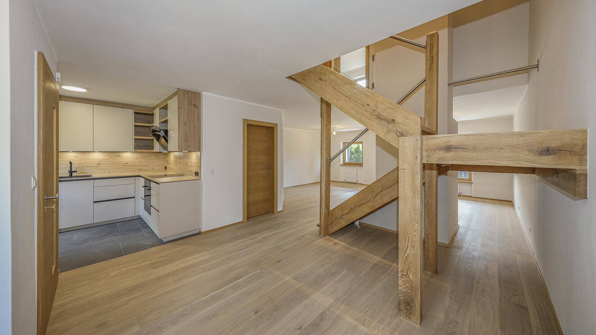 Heller Flur mit Holzboden und offener Holztreppe, führt zur Küche und weiteren Räumen.