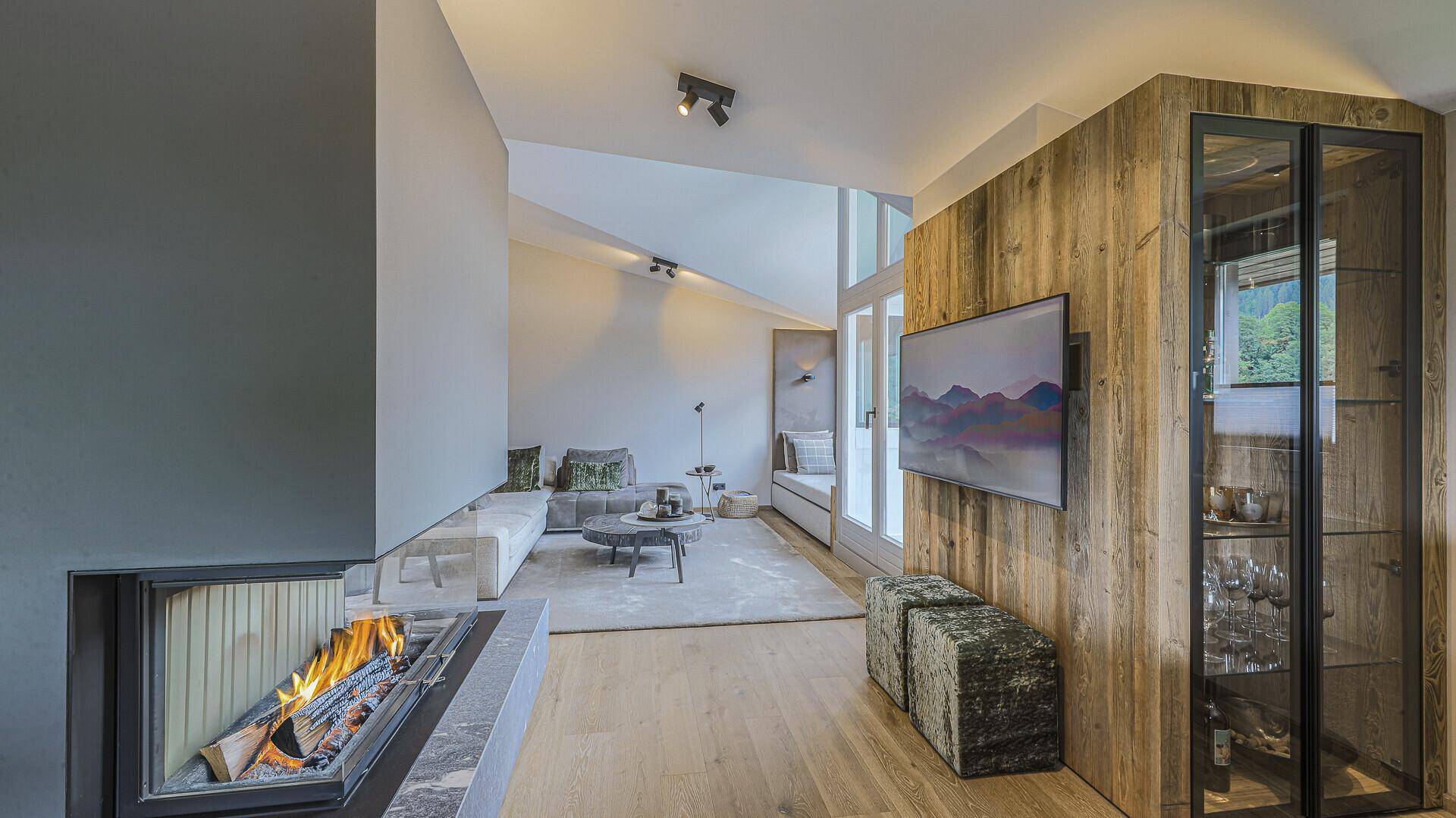 Heller Wohnbereich mit Kamin, Holzwand und großen Fenstern, die viel Tageslicht hereinlassen.