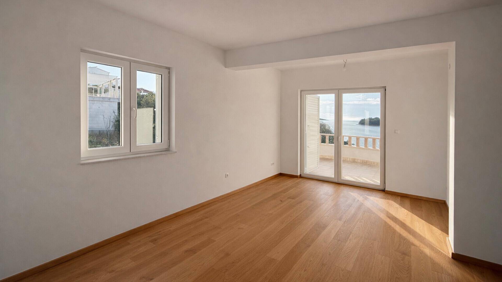 Heller, leerer Raum mit Holzboden und Zugang zu einem Balkon mit Meerblick.