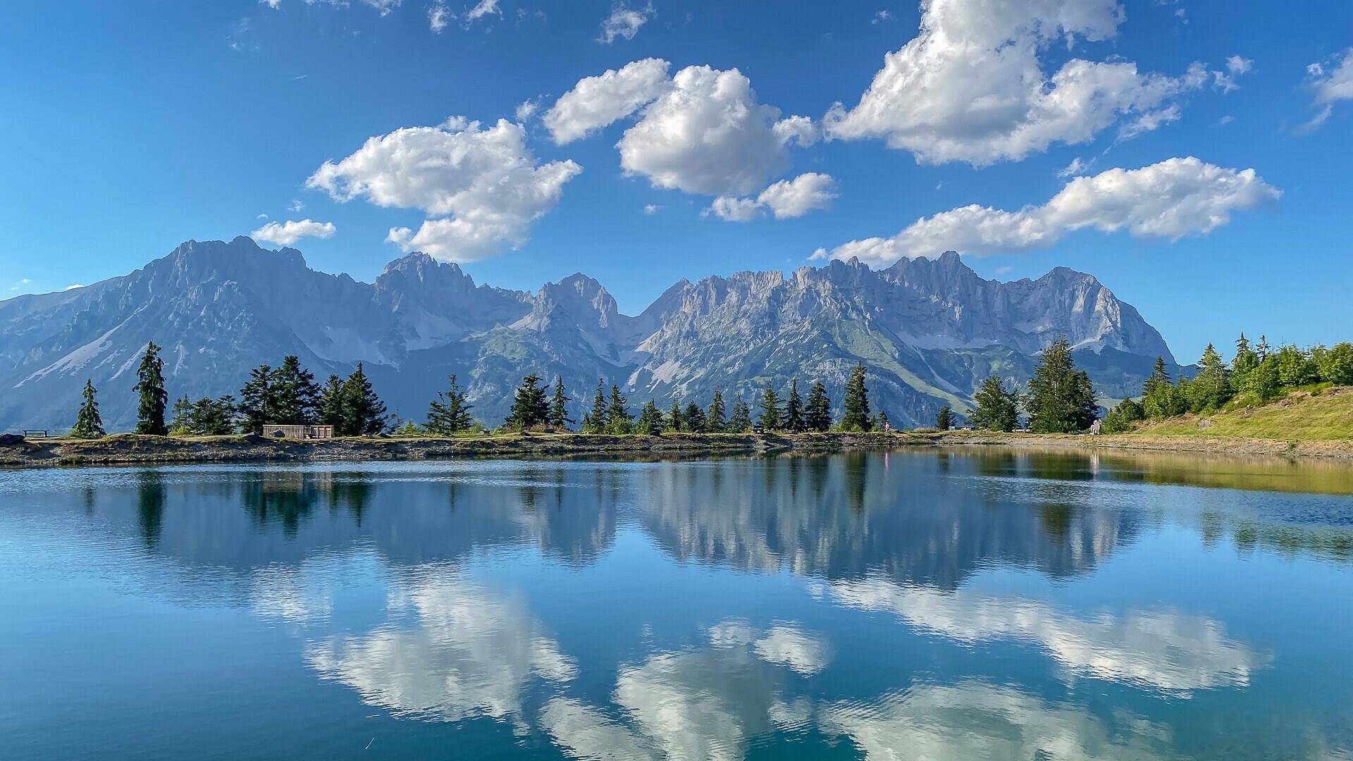 Malerischer Bergsee mit klarer Spiegelung der umliegenden Gipfel und des blauen Himmels.