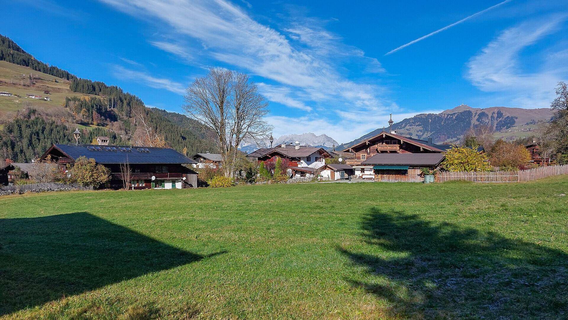 Weitläufige grüne Wiesen mit traditionellen Häusern und majestätischen Bergen im Hintergrund an einem sonnigen Tag.