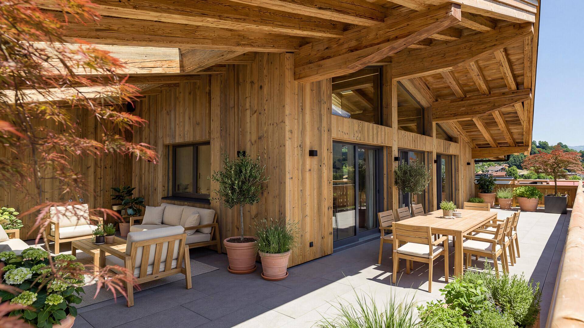 Große Terrasse mit Holzwänden, Sitzgelegenheiten und Esstisch, umgeben von Pflanzen und Bergblick.
