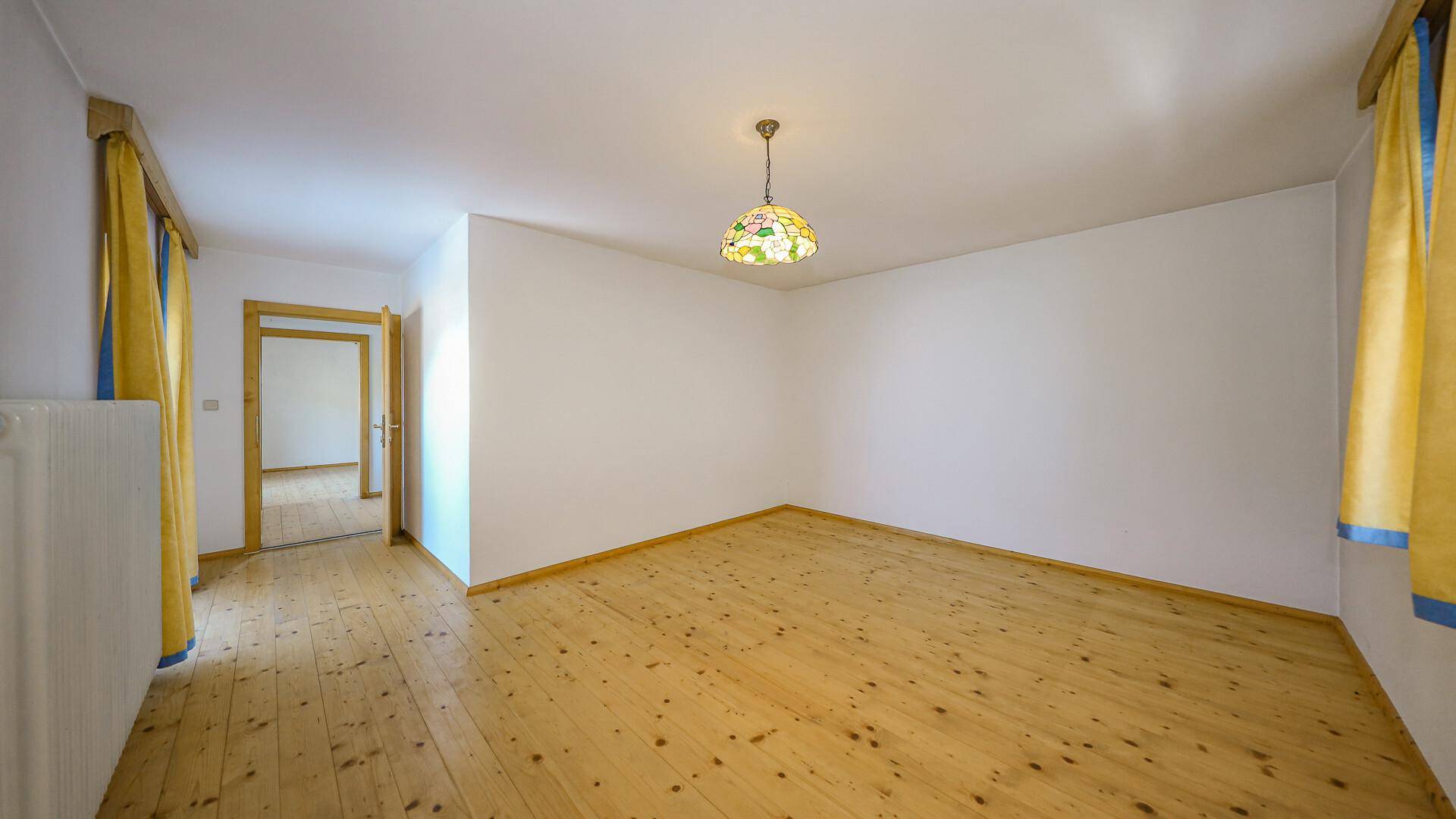 Helles Zimmer mit Holzdielenboden, weißen Wänden und einem bunten Deckenlicht.