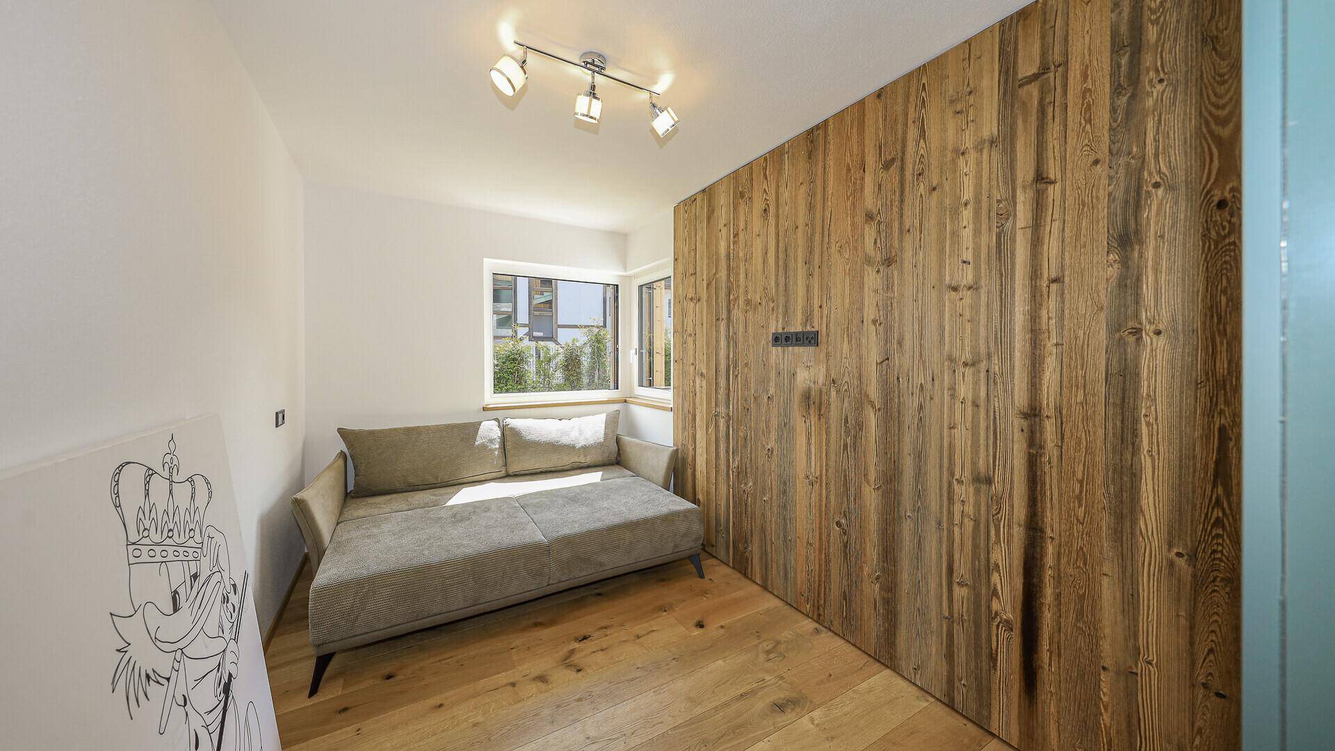 Kleines Zimmer mit Holzboden, Schlafsofa und Fenster mit Blick ins Grüne.