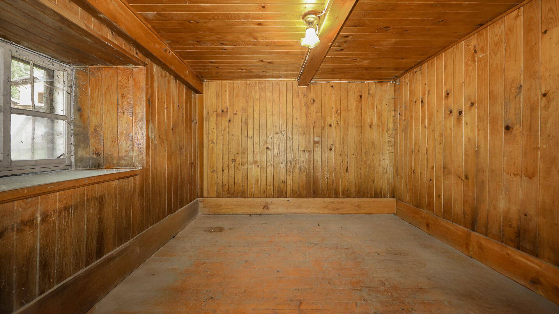 Einfacher Raum im Untergeschoss mit Holzverkleidung und kleinem Fenster.