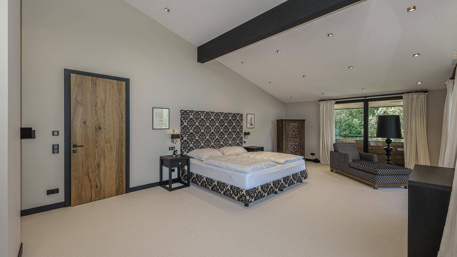 Helles Schlafzimmer mit Teppichboden, Dachschräge und dunklen Deckenbalken.