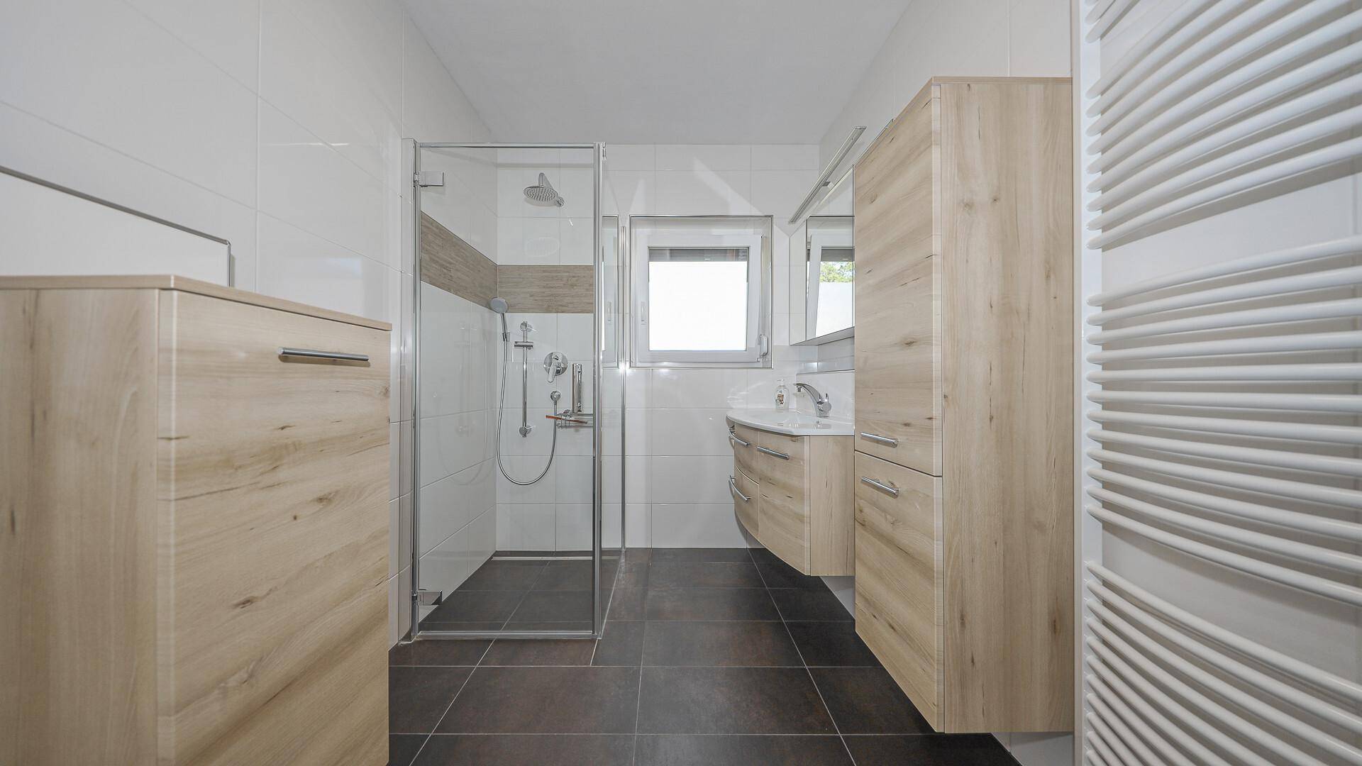 Modernes Badezimmer mit ebenerdiger Dusche, Holzmöbeln und beheiztem Handtuchhalter.