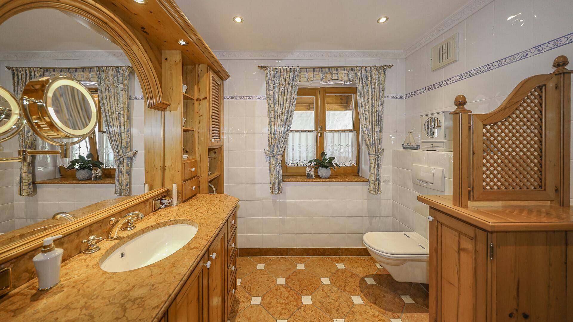 Traditionelles Badezimmer mit Holzmöbeln, Einzelwaschbecken und Fenster, das viel Tageslicht hereinlässt.