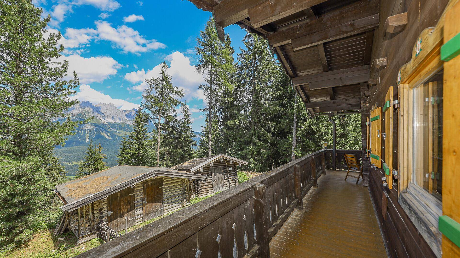 Holzverkleideter Balkon mit Blick auf die Berge und rustikale Nebengebäude, ideal zum Entspannen.