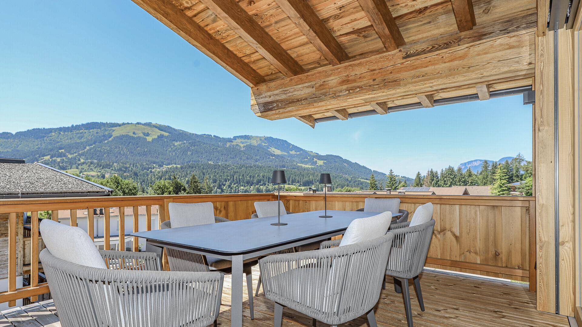 Geräumiger Holzbalkon mit Esstisch und Stühlen, bietet einen weiten Blick auf die Berge.