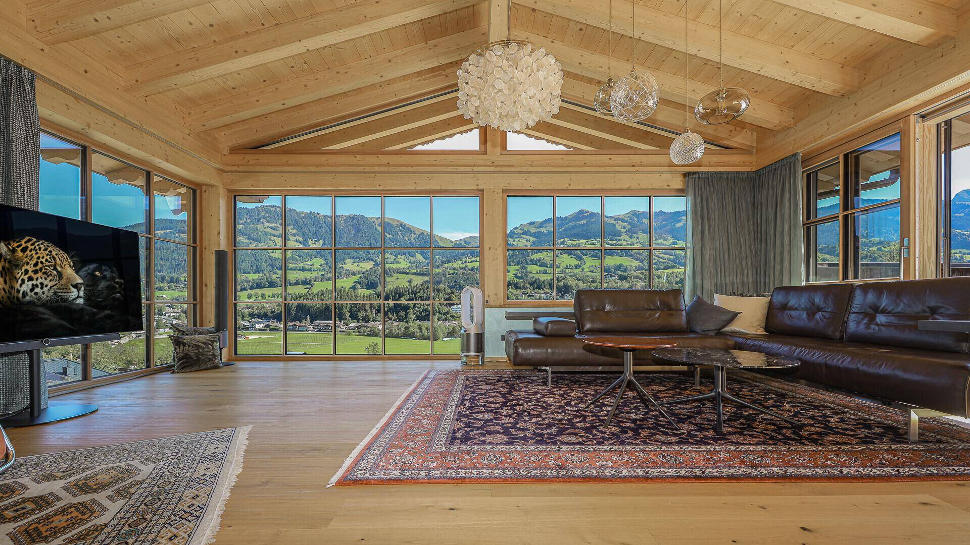 Geräumiges Wohnzimmer mit Holzbalkendecke, großen Fenstern und atemberaubendem Bergblick.