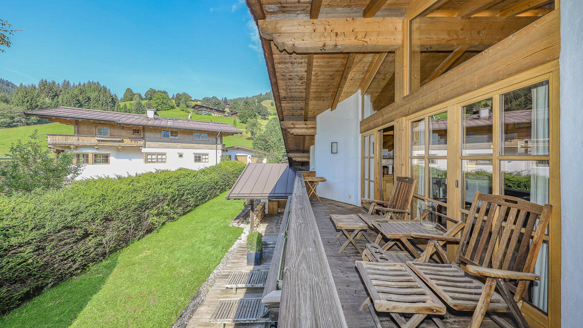 Großer Holzbalkon mit Liegestühlen und weitem Blick auf die grüne Landschaft.