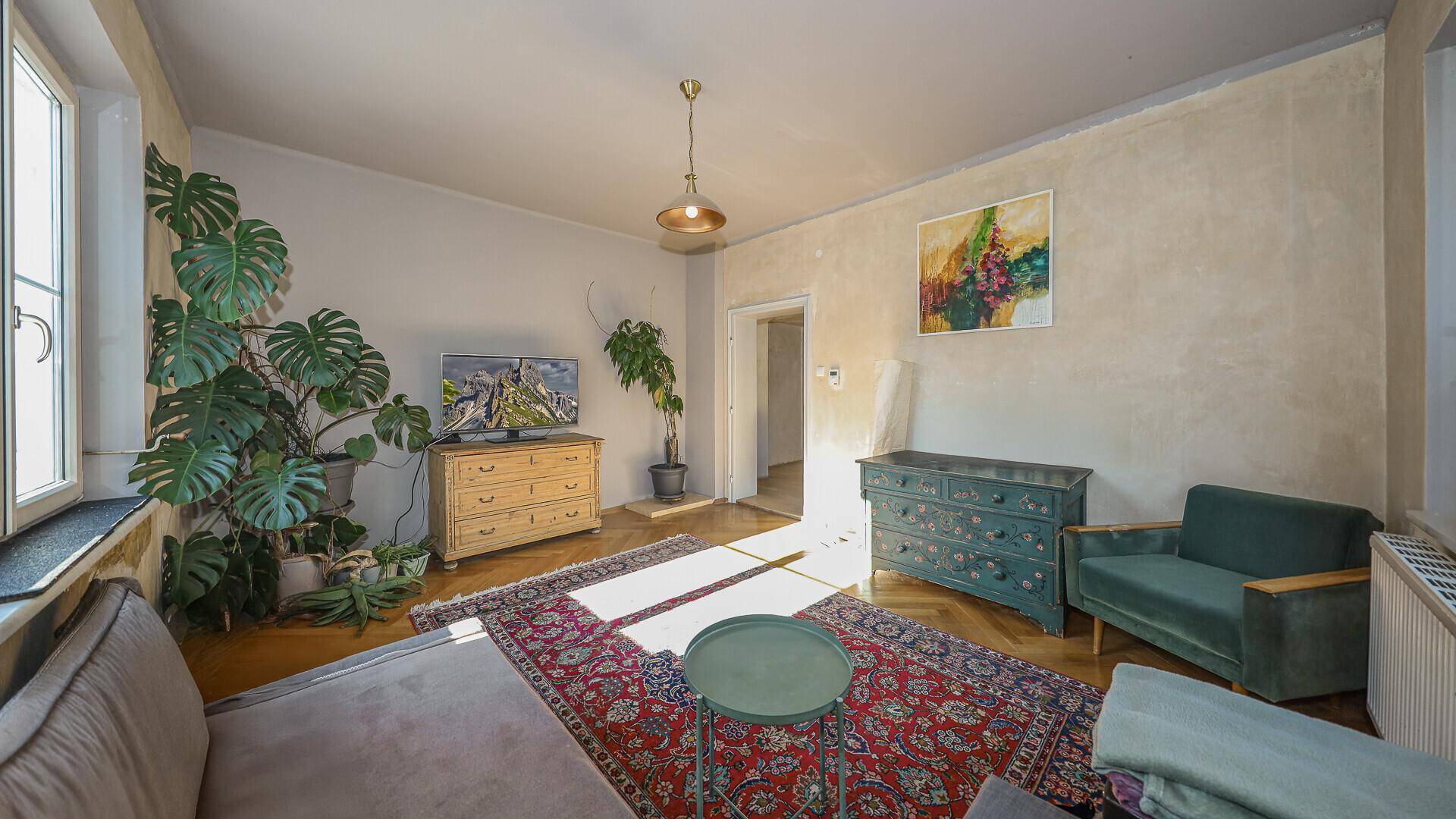 Helles Wohnzimmer mit Parkettboden, großem Fenster und traditionellem Teppich.