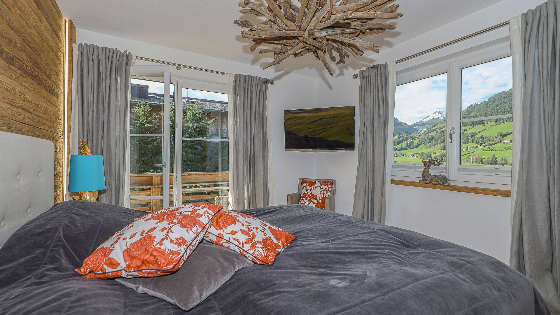 Gemütliches Schlafzimmer mit Holzwand, großem Bett und Fenstern mit Bergblick.