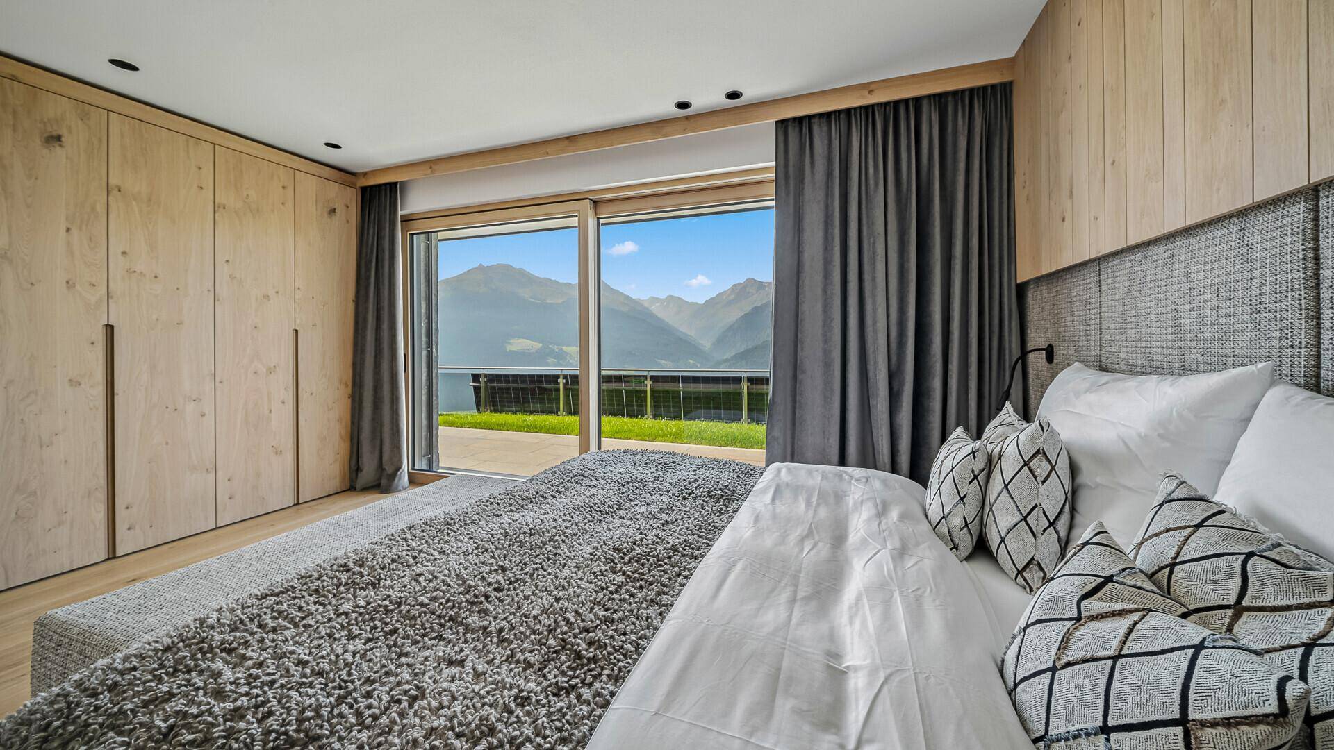 Schlafzimmer mit Holzwand, Einbauschränken und Zugang zur Terrasse mit Bergblick.