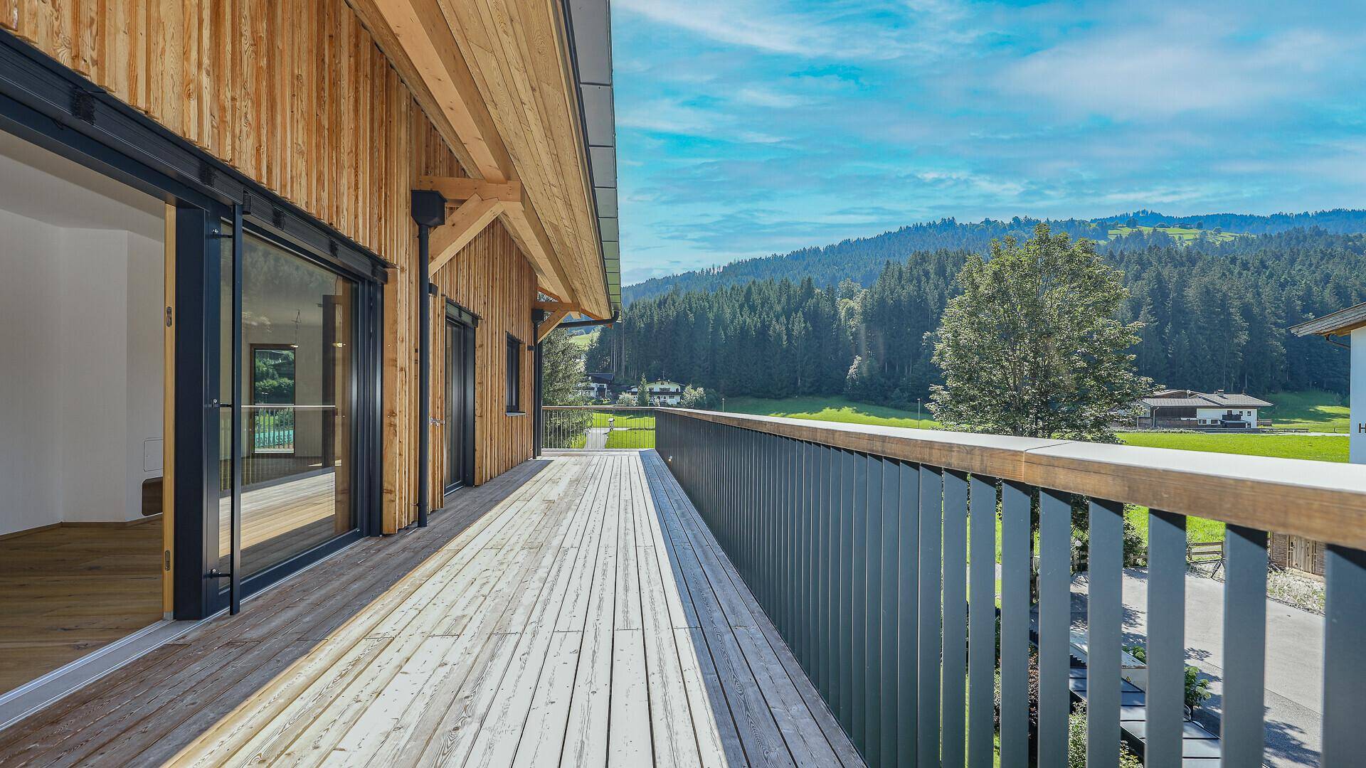 Großer Holzbalkon mit Metallgeländer und weitem Blick auf die umliegende Berglandschaft.