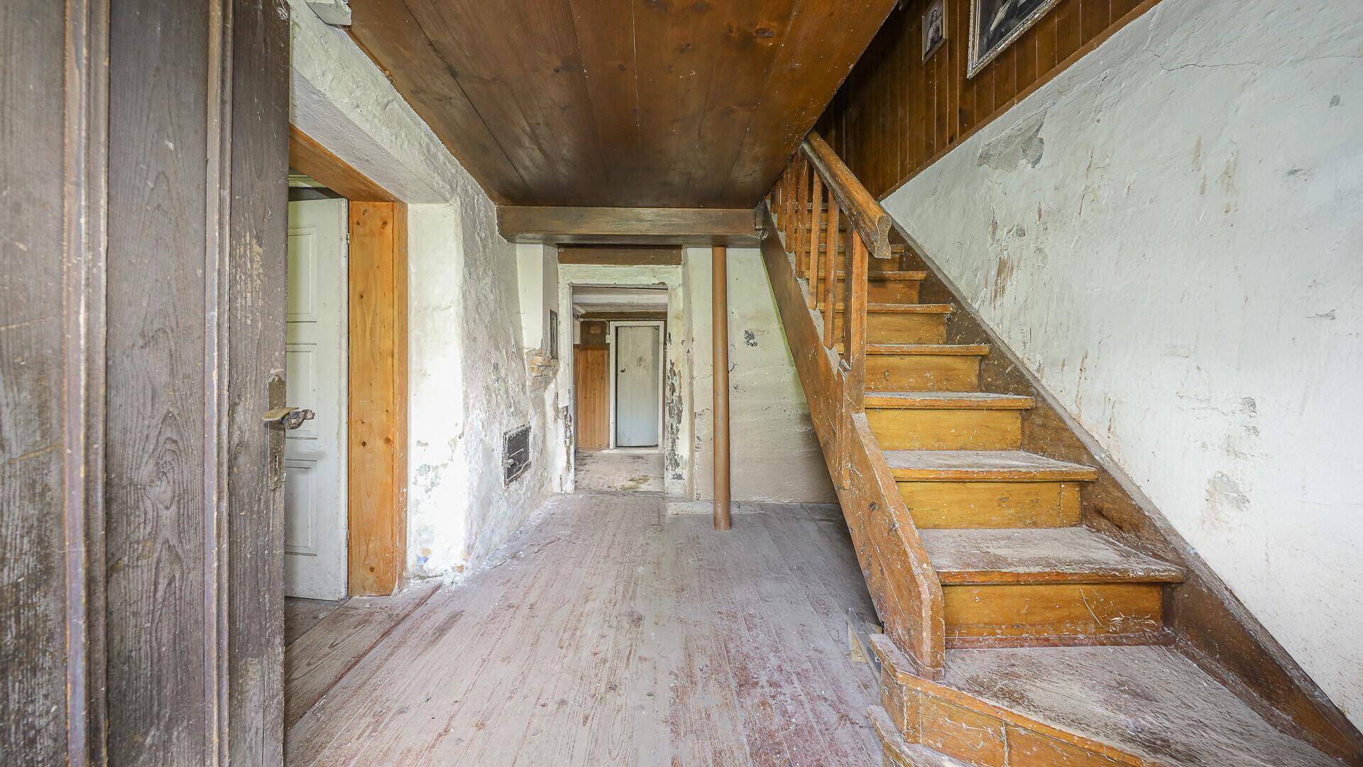 Rustikaler Flur mit Holztreppe und Holzdielenboden, der in weitere Räume führt.