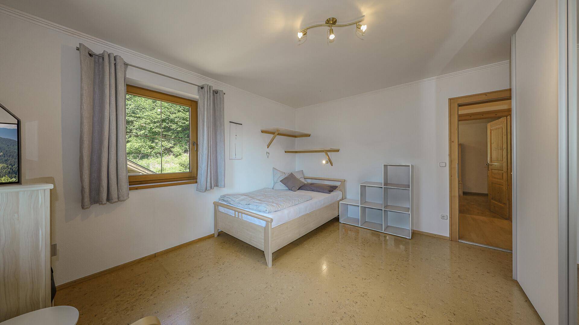 Einfaches Schlafzimmer mit Einzelbett, Holzdecke und Fenster mit Blick ins Grüne.