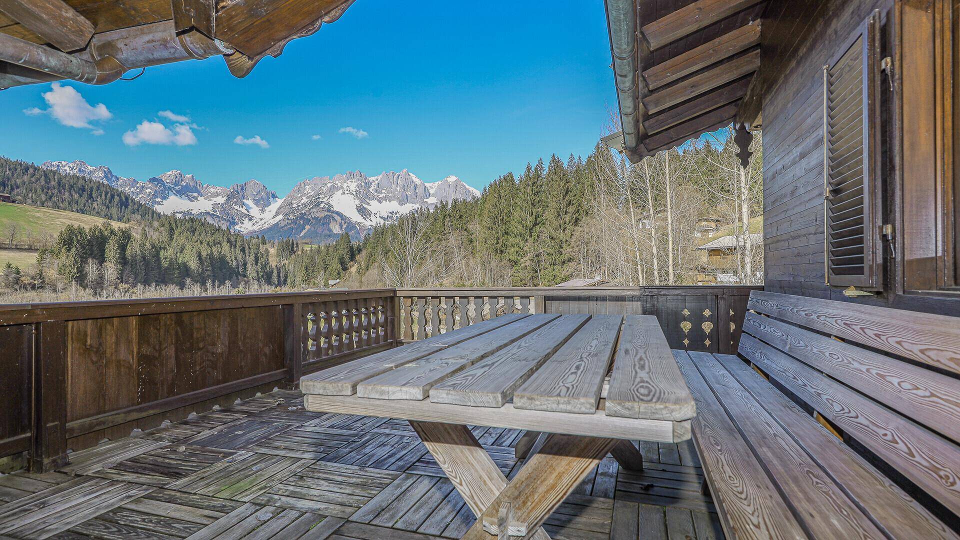 Großer Holzbalkon mit Esstisch und Sitzbank, bietet einen atemberaubenden Bergblick.