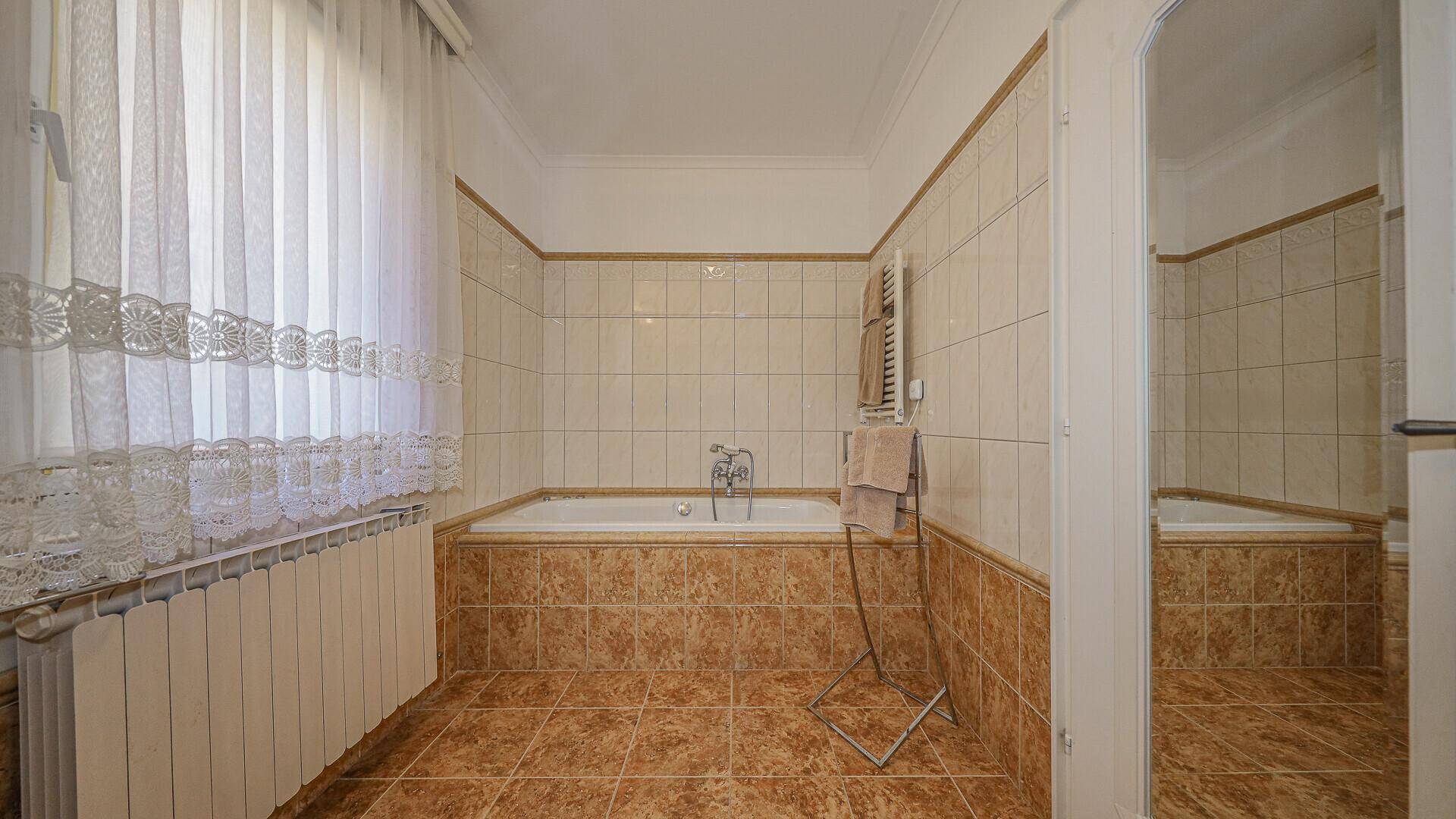 Badezimmer mit Badewanne, Fliesenboden und Fenster, in traditionellem Design.
