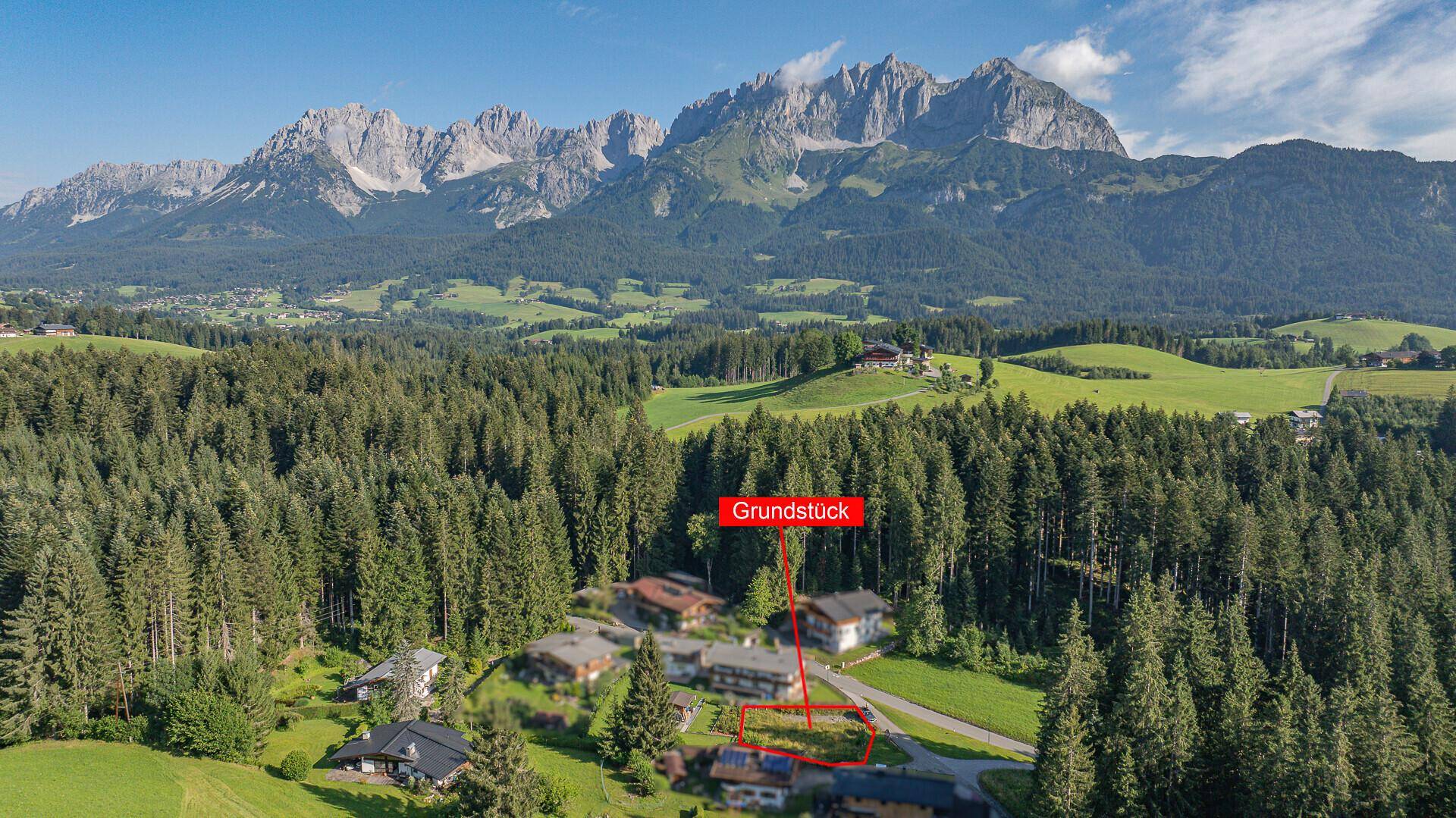 Luftaufnahme eines Baugrundstücks in einer malerischen Berglandschaft mit Wald.