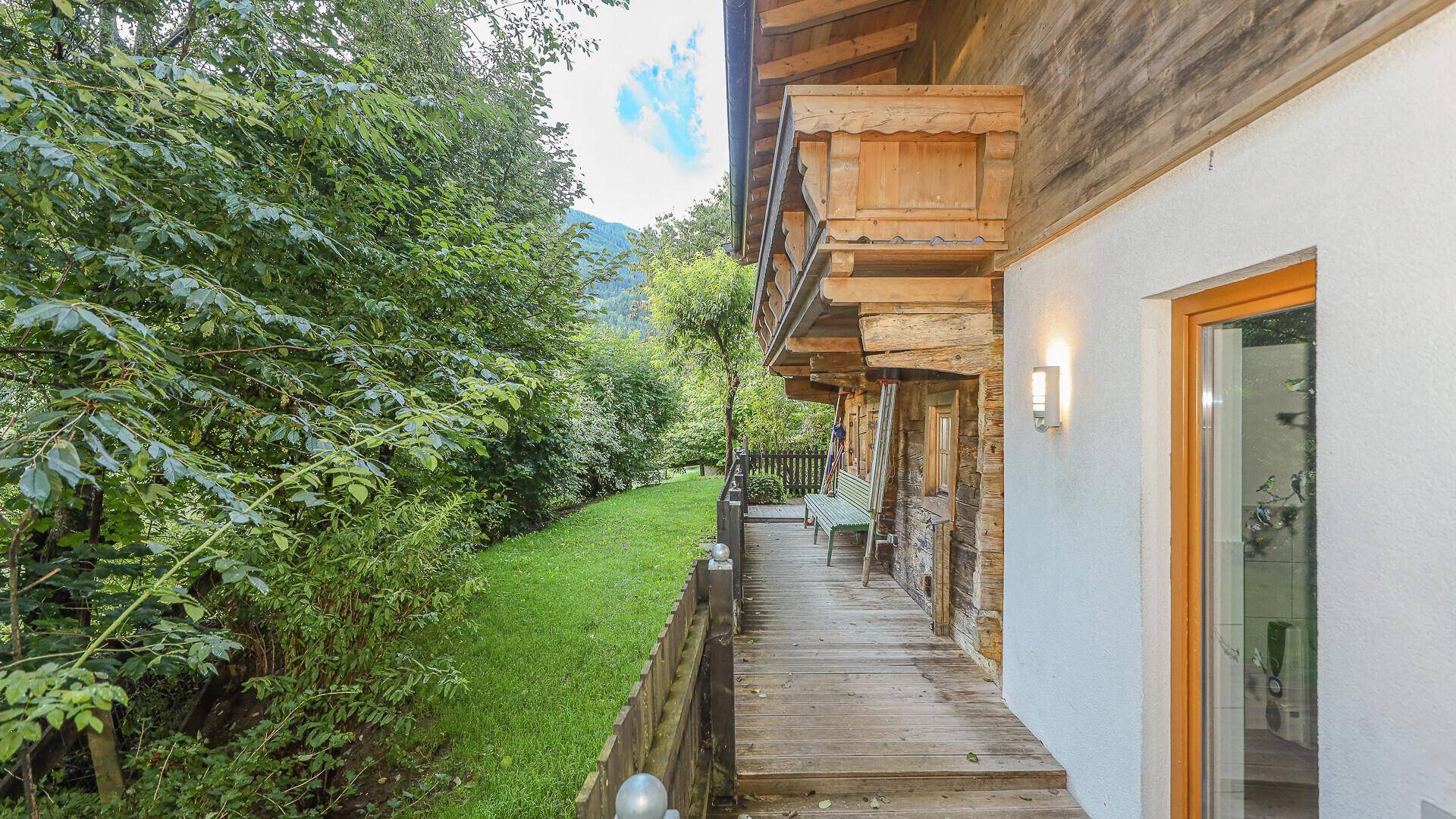 Seitliche Holzterrasse mit Zugang zum Garten und Blick auf die grüne Umgebung.
