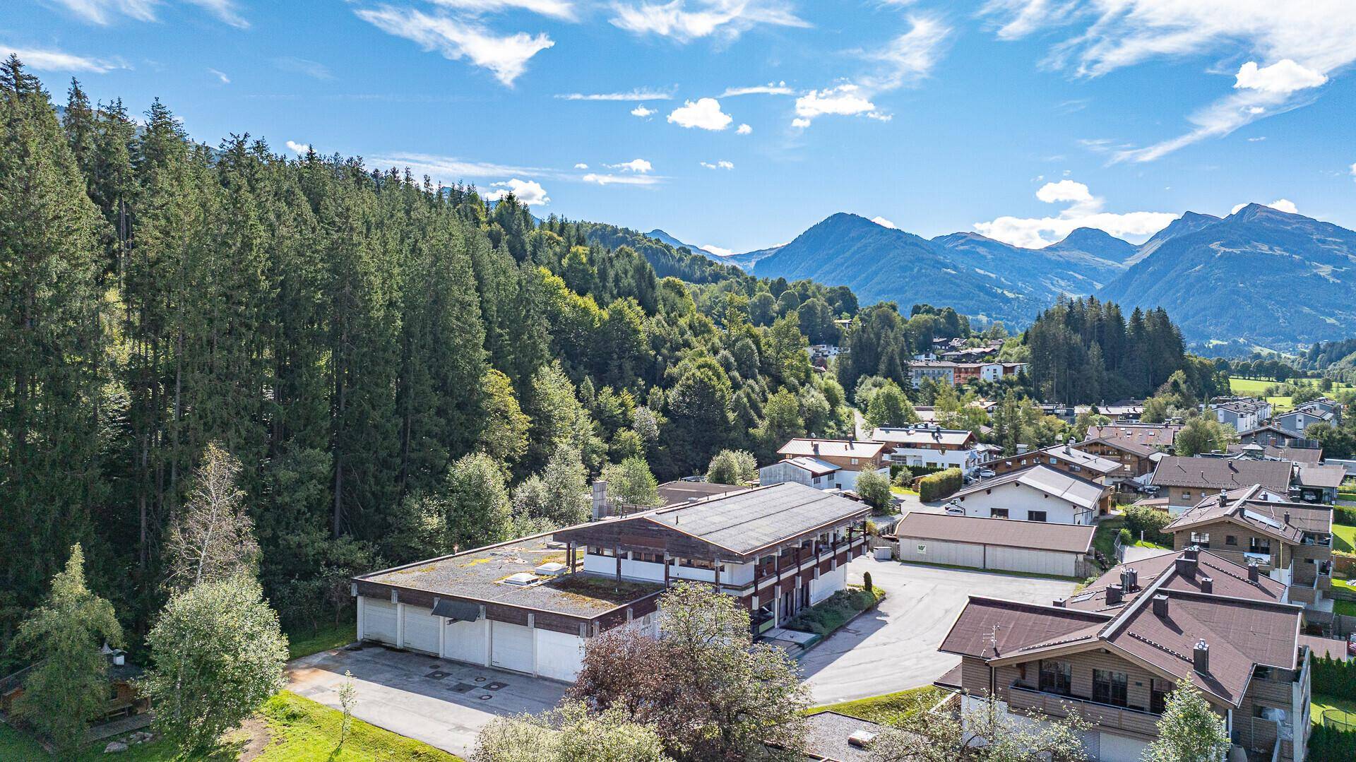 Luftaufnahme des Gebäudes mit Flachdach, umgeben von dichtem Wald und sanften Hügeln.