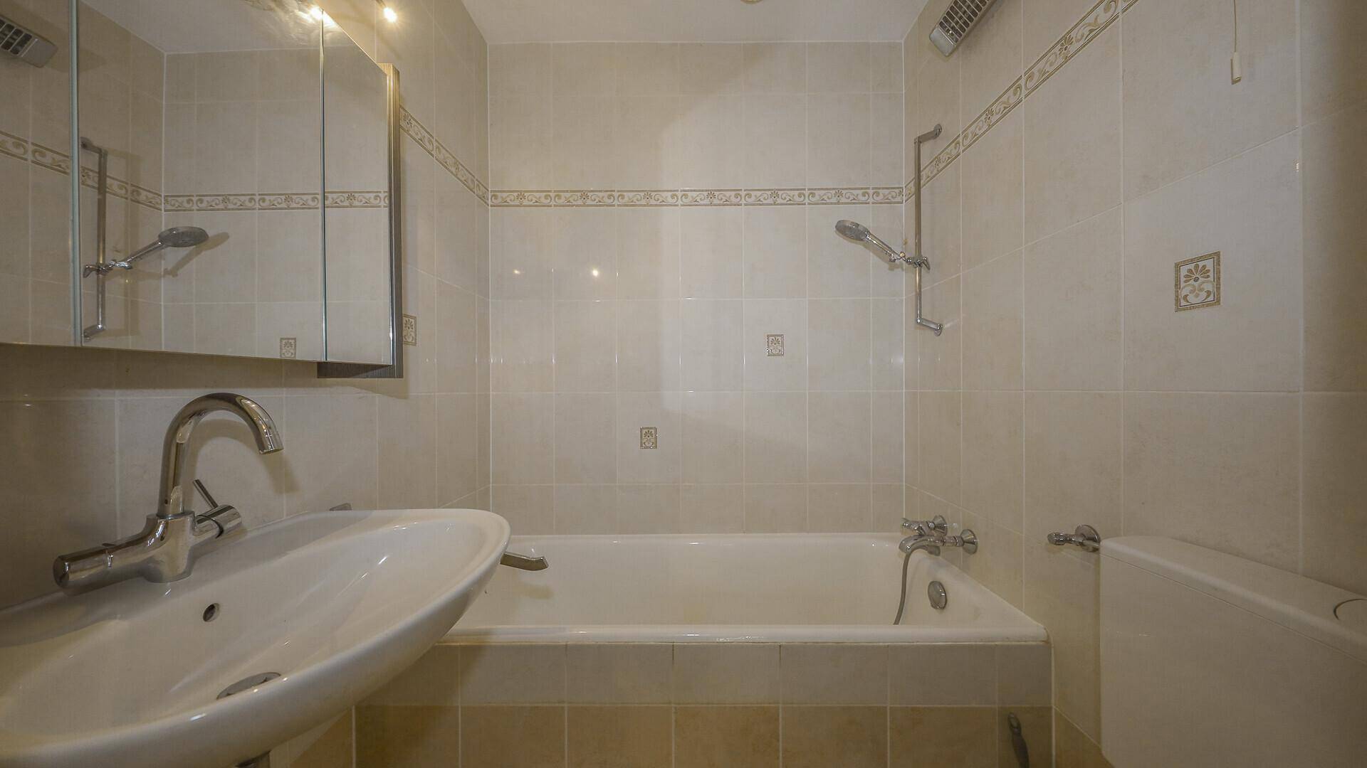 Badezimmer mit beigefarbenen Fliesen, Badewanne mit Duschfunktion und Spiegelschrank.