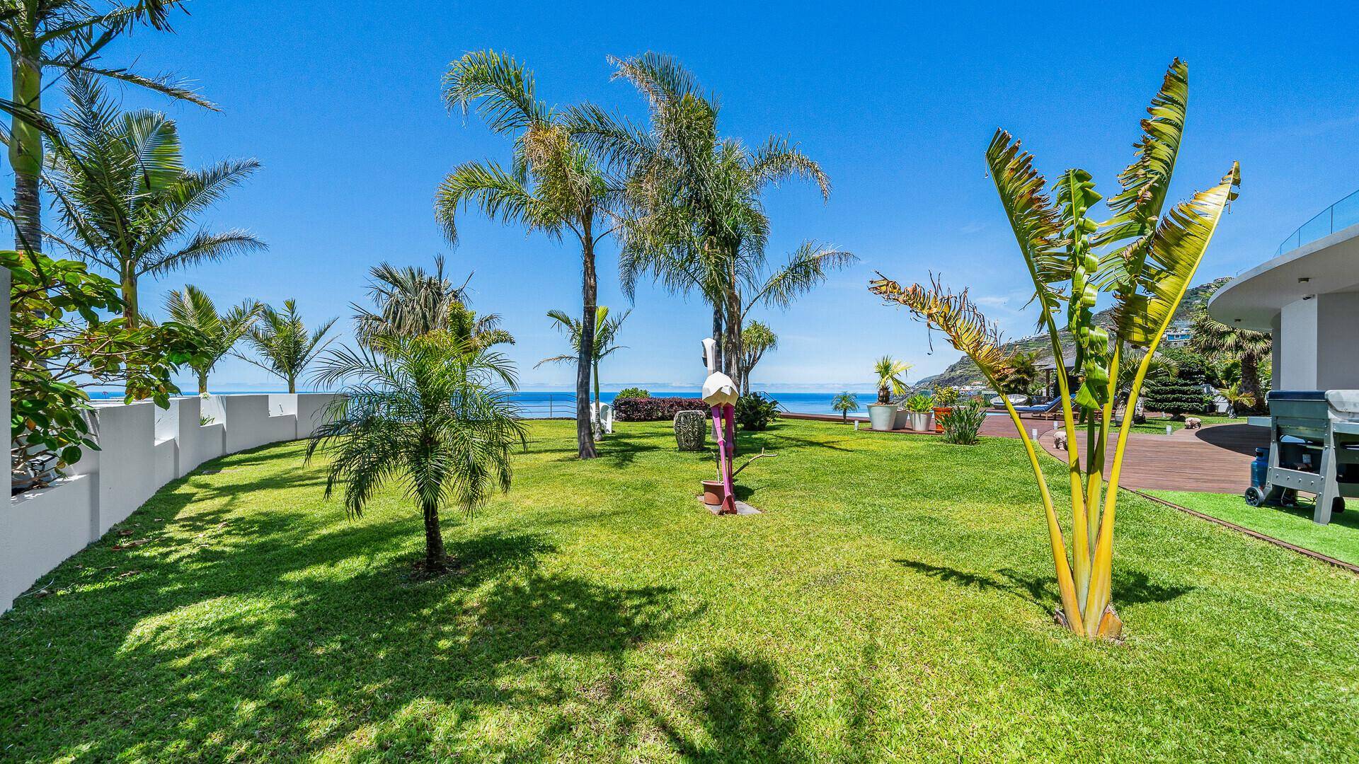 Gepflegter Garten mit Rasenflächen, Palmen und einem weiten Blick auf das Meer.