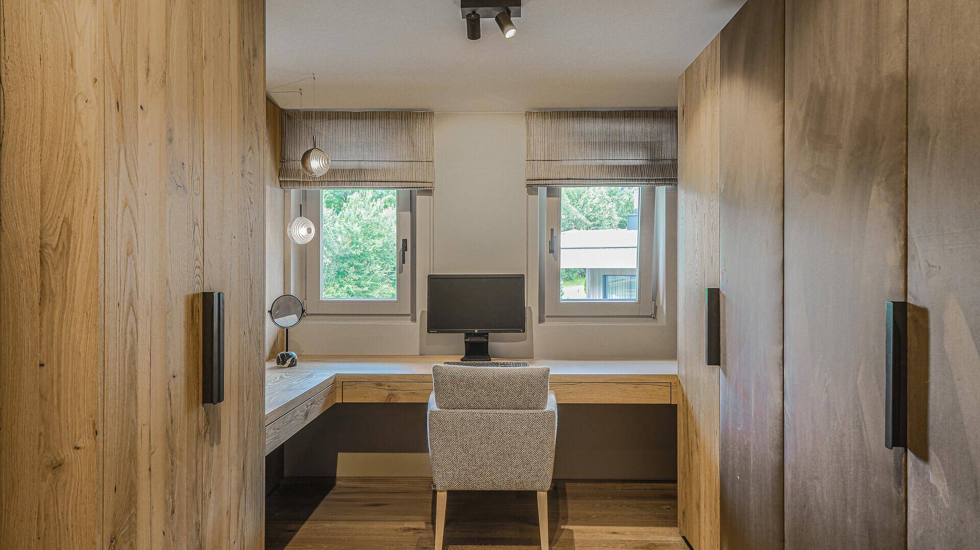 Funktionales Büro mit Schreibtisch, Einbauschränken und Fenstern mit grüner Aussicht.