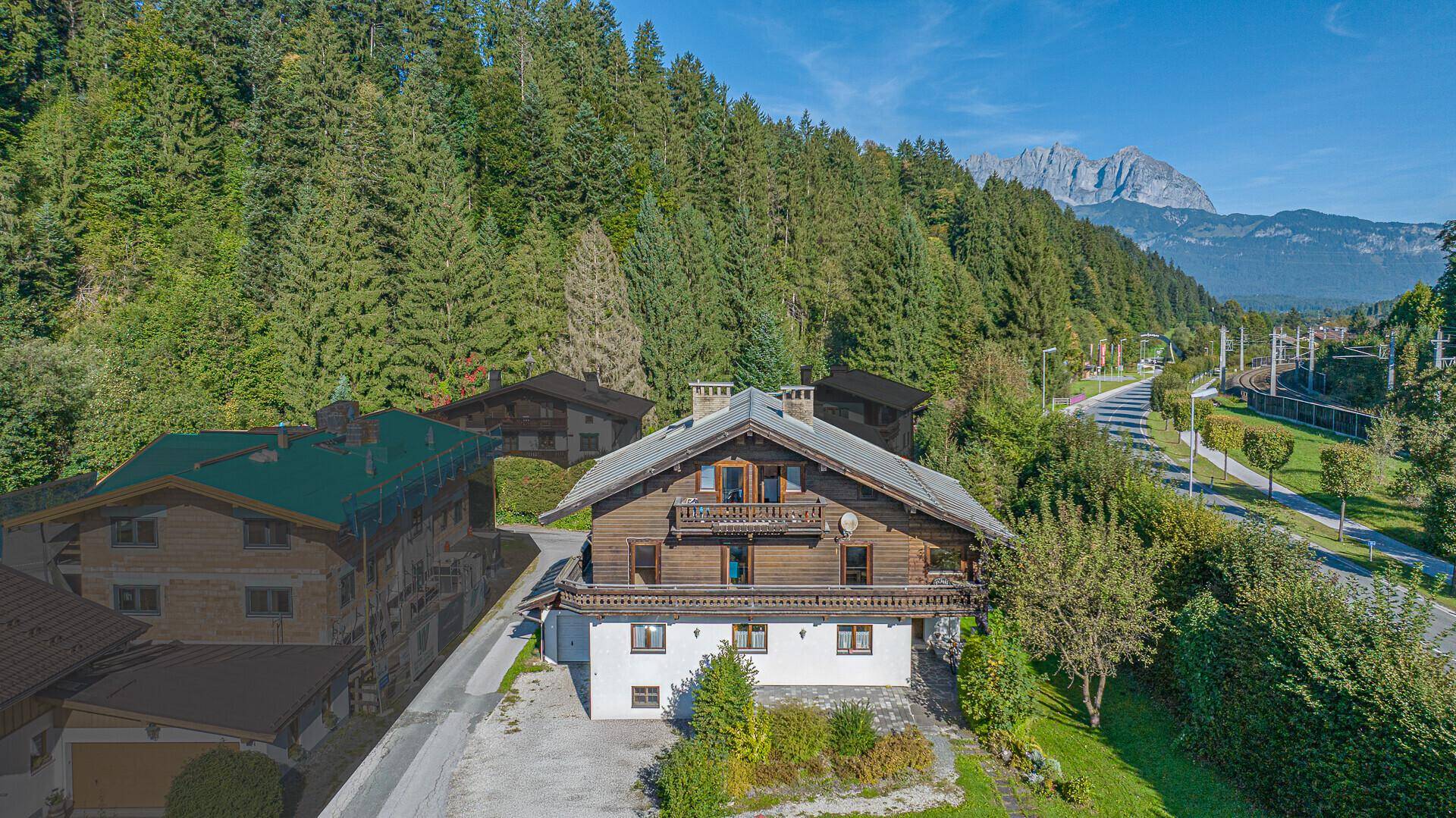 Luftaufnahme eines traditionellen Holzhauses mit weißem Sockel und beeindruckendem Bergblick.