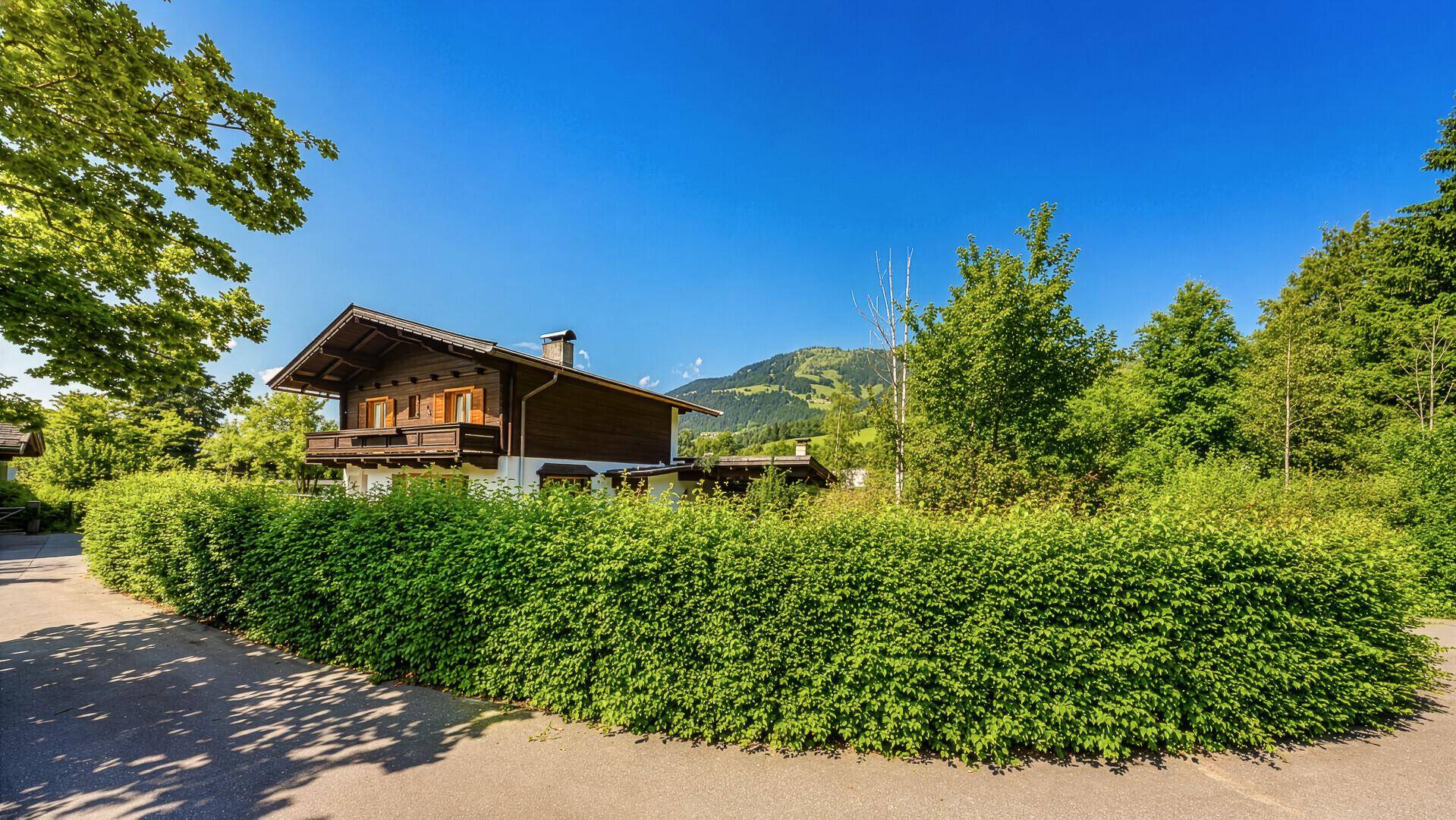 Traditionelles Chalet, umgeben von einer dichten Hecke, mit weitem Blick auf die Berge.