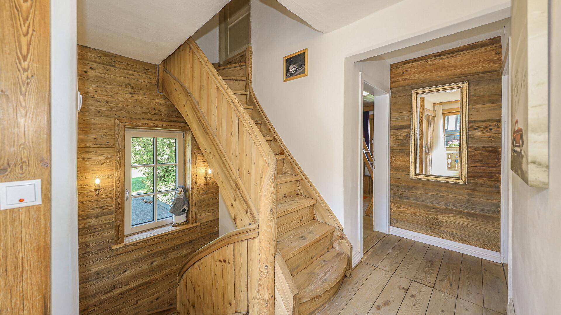 Holztreppe mit Fenster und Spiegel, die die oberen Etagen verbindet.