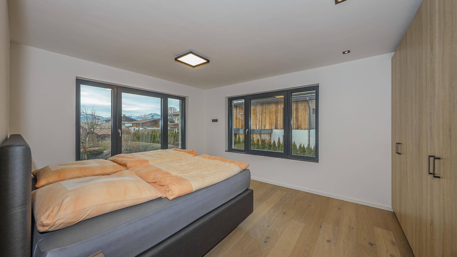 Gemütliches Schlafzimmer mit Doppelbett, Holzboden und Fenstern mit Blick ins Grüne.