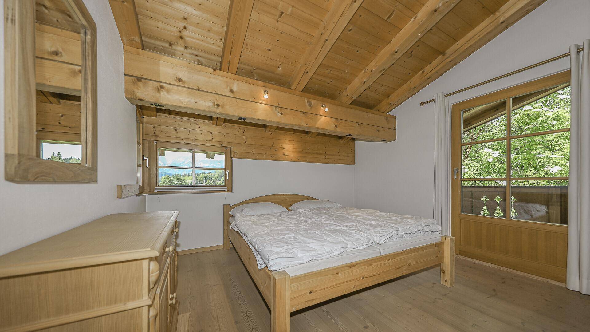 Helles Schlafzimmer mit Holzbalkendecke, Holzbett und direktem Zugang zum Balkon.