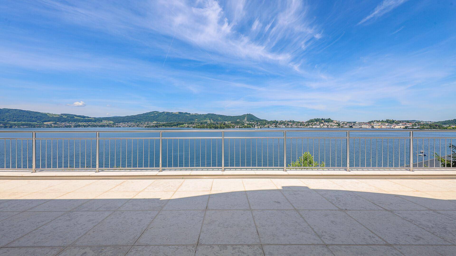 Weitläufige Terrasse mit Fliesenboden und Edelstahlgeländer, bietet einen spektakulären Seeblick.