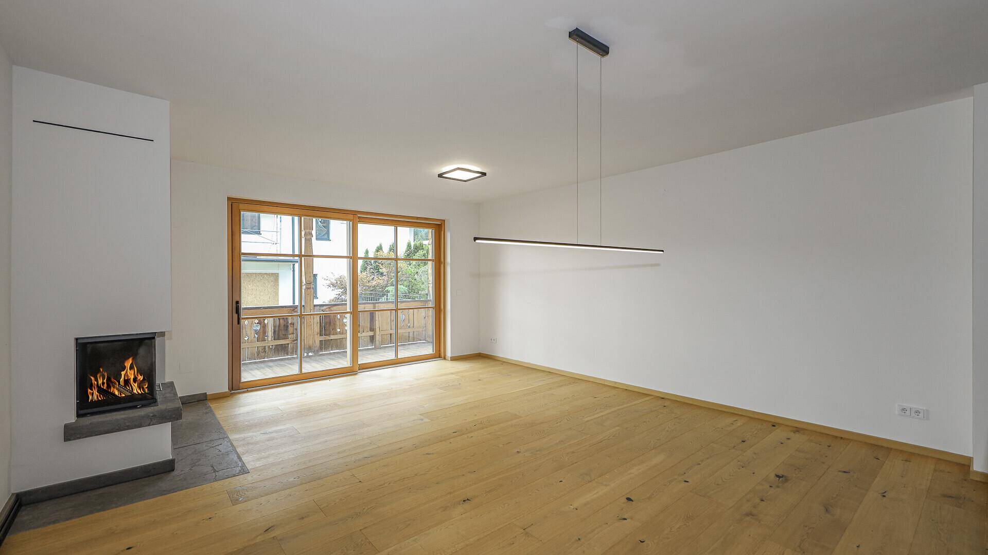 Geräumiger Wohnbereich mit Holzboden, Kamin und Zugang zu einem Balkon.