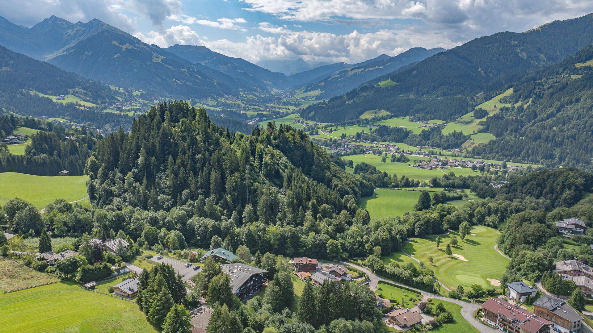 Weitläufige Panoramaaufnahme eines grünen Tals mit bewaldeten Hügeln und majestätischen Bergen.