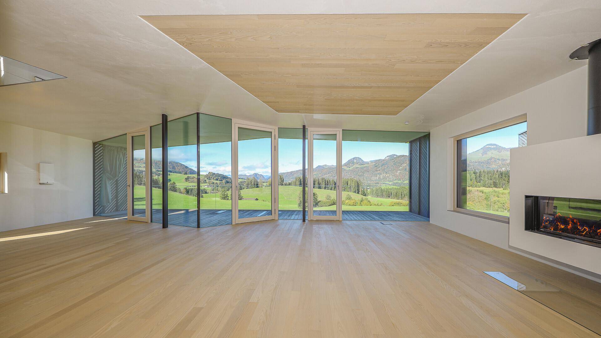Heller, unmöblierter Wohnbereich mit Holzboden, Kamin und weitem Blick auf die grüne Landschaft.