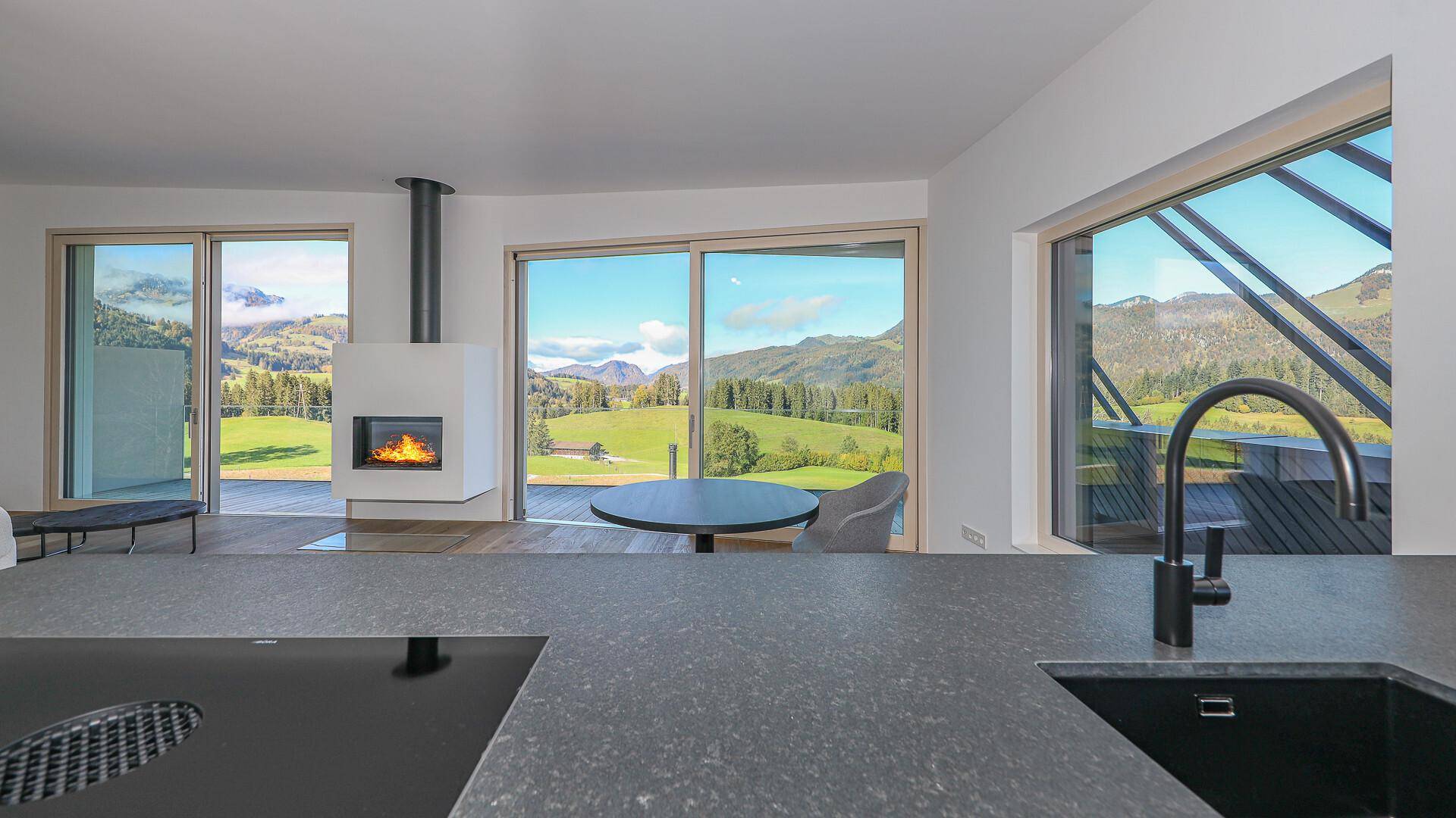 Moderne Küchenzeile mit dunkler Arbeitsplatte und Spüle, mit Blick auf den Wohnbereich und die Berge.