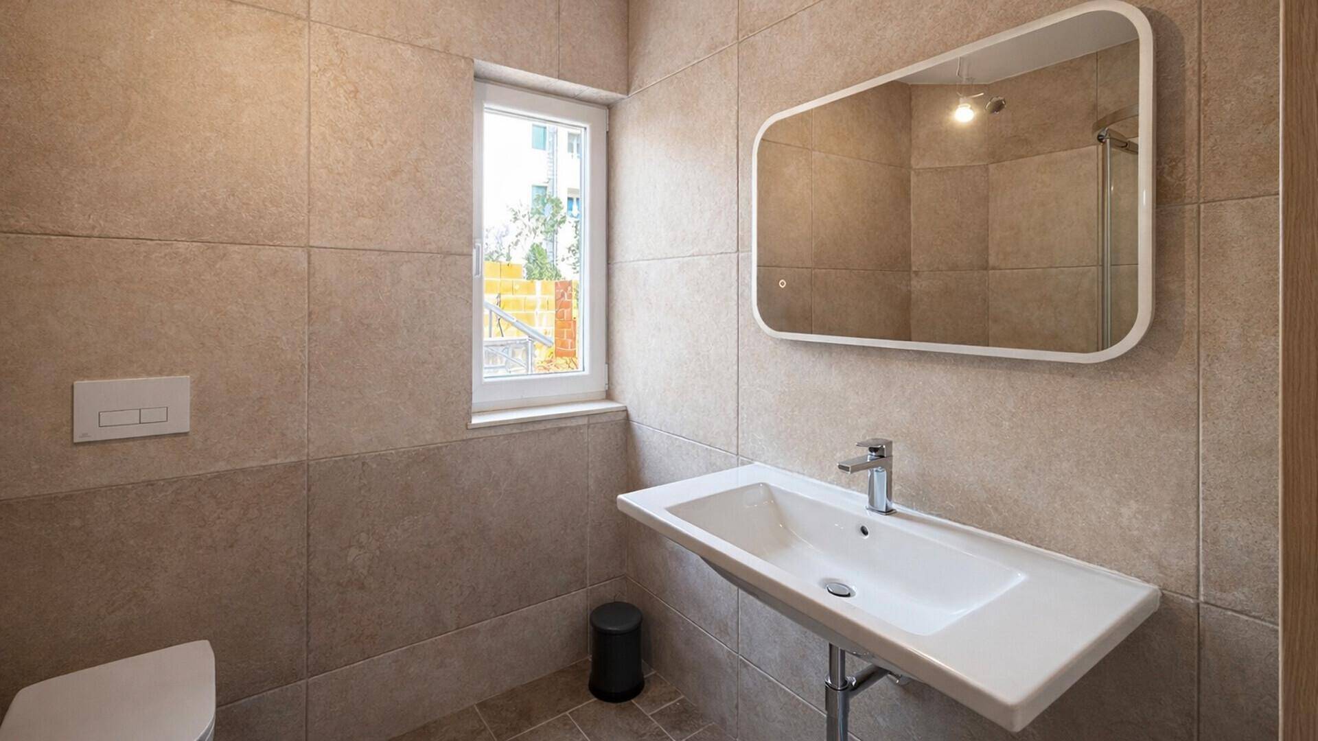 Helles Badezimmer mit modernem Waschbecken, beleuchtetem Spiegel und Fenster für Tageslicht.