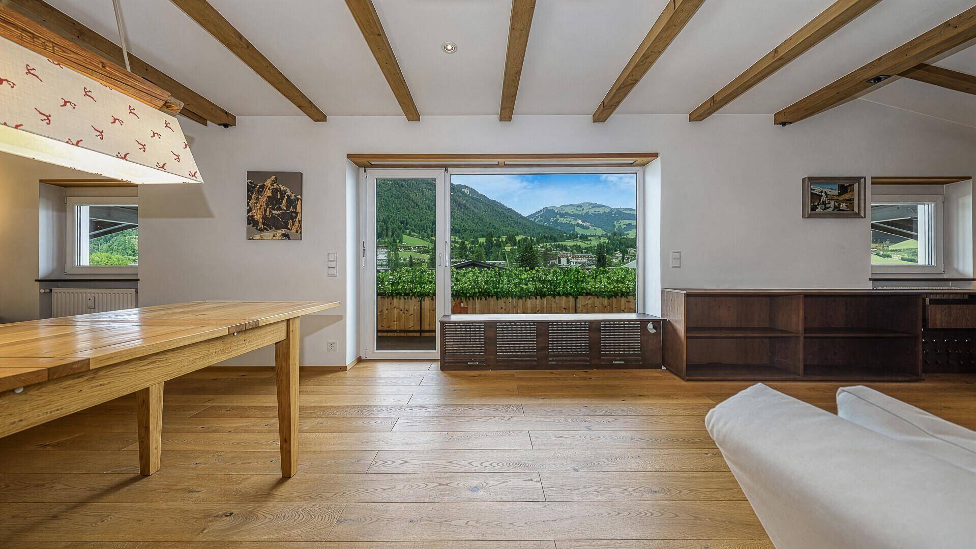 Geräumiger Wohn- und Essbereich mit Holzbalken, Holzboden und großem Fenster mit Bergblick.