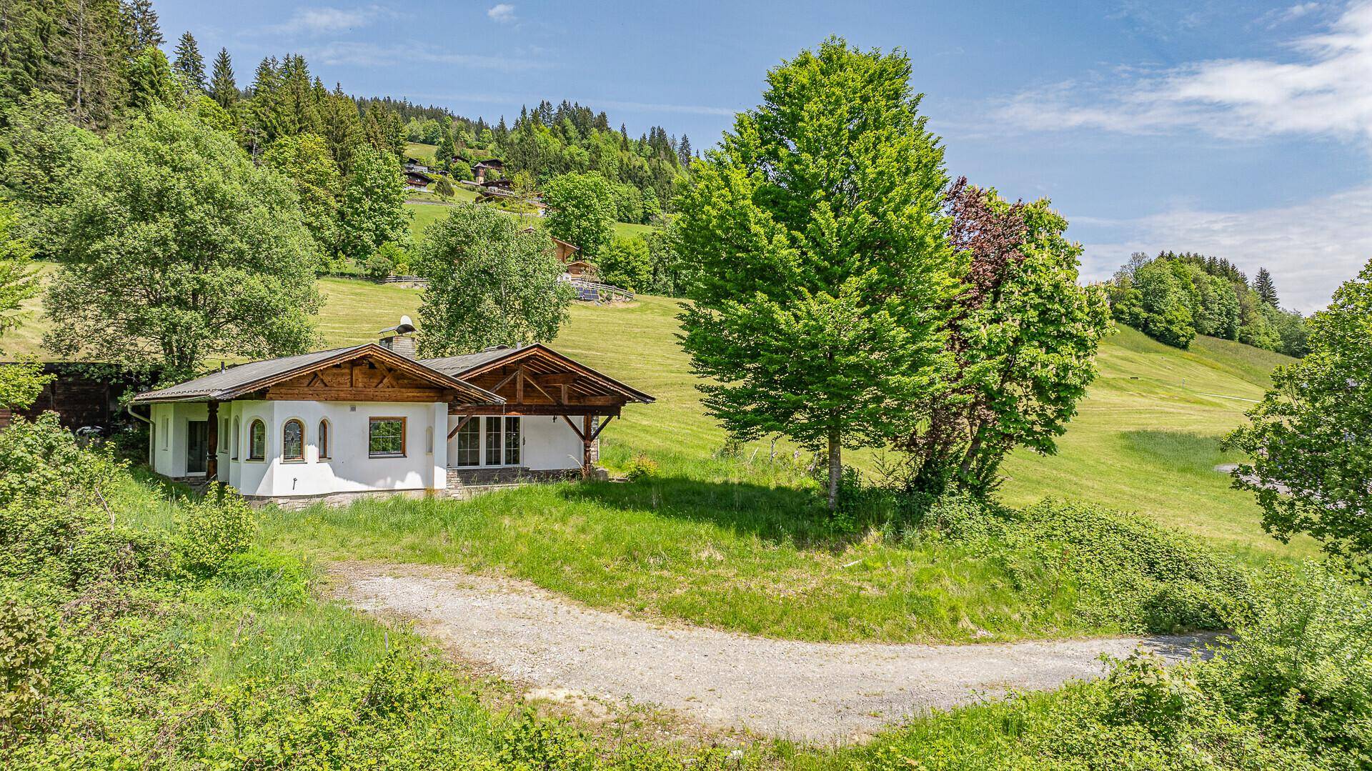Charmantes Haus in ländlicher Umgebung, umgeben von grünen Wiesen und hohen Bäumen.