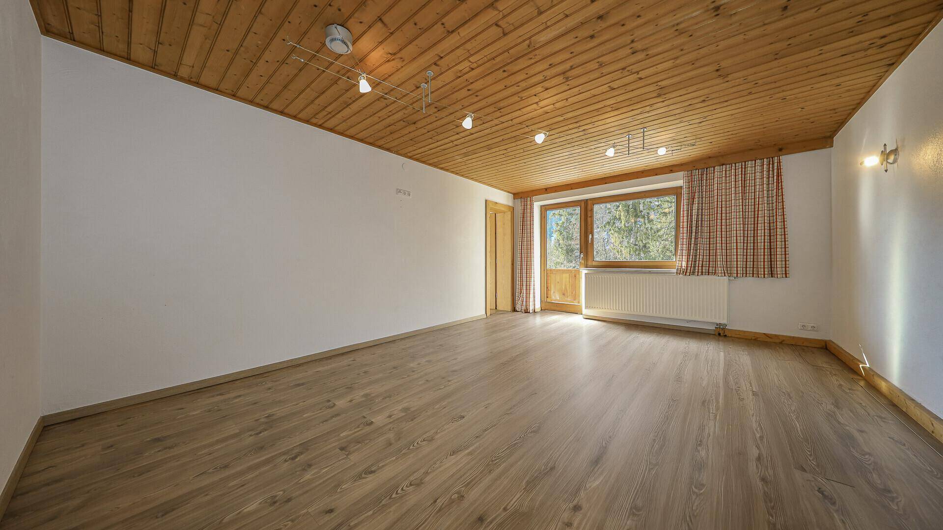 Lichtdurchflutetes Zimmer mit Holzboden, Holzdecke und Zugang zum Balkon.