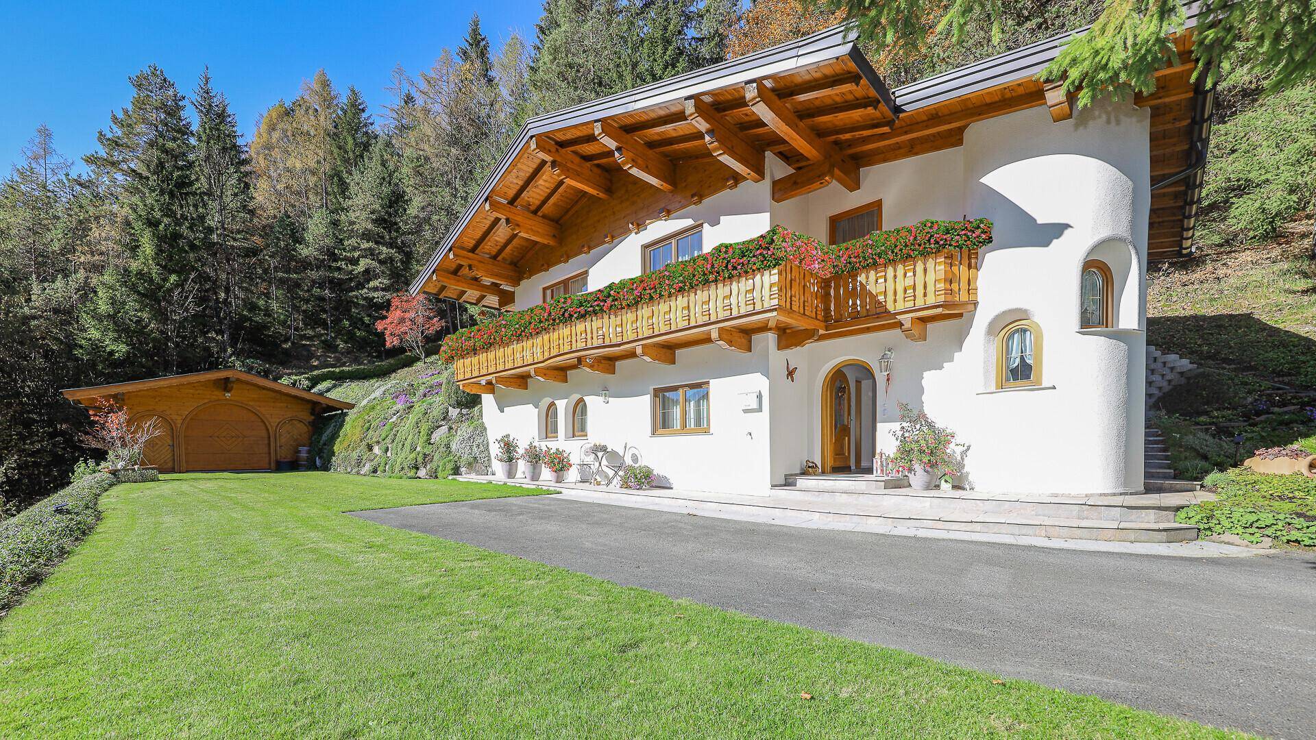 Traditionelles Alpenchalet mit weißer Fassade, Holzbalkonen und gepflegtem Vorgarten unter blauem Himmel.